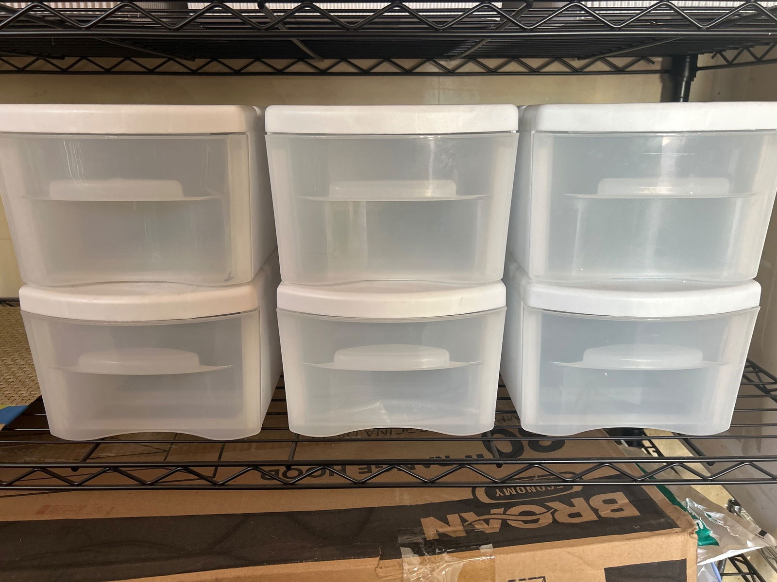 Six Stackable Plastic Storage Drawers with White Lids: Six clear plastic storage drawers with white lids, featuring stackable design for organization. Each drawer has a curved handle for easy use. Made from durable plastic material for lightweight stackin