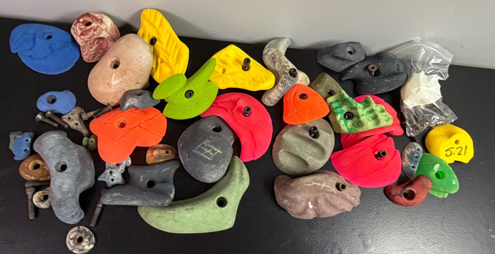 Climbing Wall Pegs With Mixed Colors and Styles: Climbing wall pegs in multiple colors and sizes. Includes bolts and hardware for installation and use, as shown. Each piece features a textured surface to aid grip, with unique shapes for varied climb