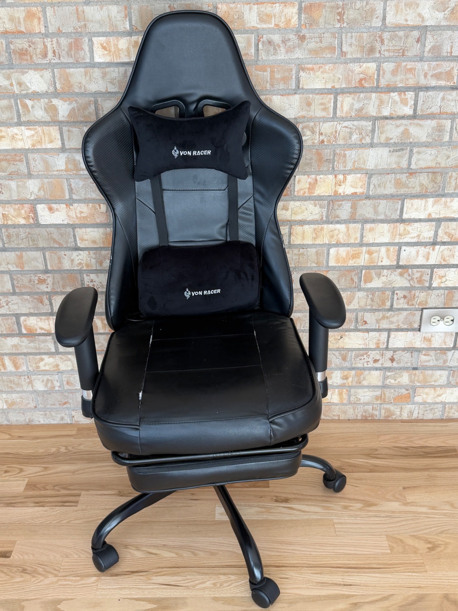 Von Racer Gaming Chair Model 8280 With Accessories: Von Racer gaming chair, model 8280, featuring a high-back design, adjustable armrests, and ergonomic lumbar and neck pillows. Made from black faux leather with some visible wear and tear noted on the