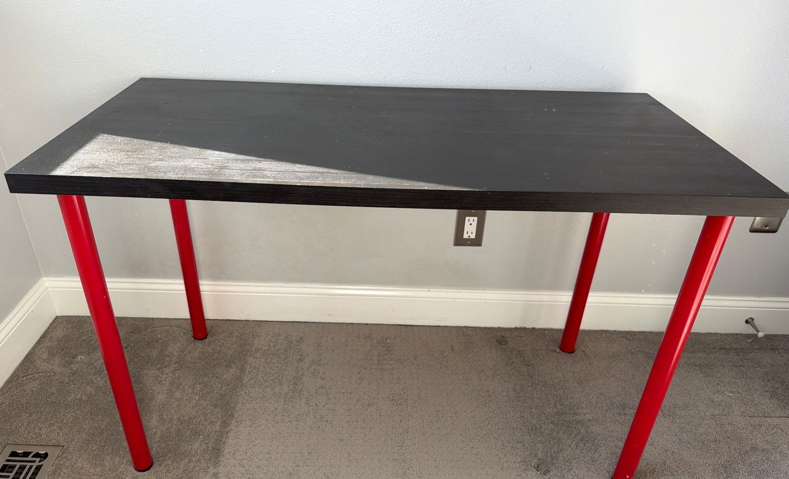IKEA Rectangular Table with Black Top and Red Legs: Rectangular table featuring a black tabletop with a smooth finish and vibrant red cylindrical metal legs. The table is sturdy and presents a clean and modern design suitable for various uses. Dimensio