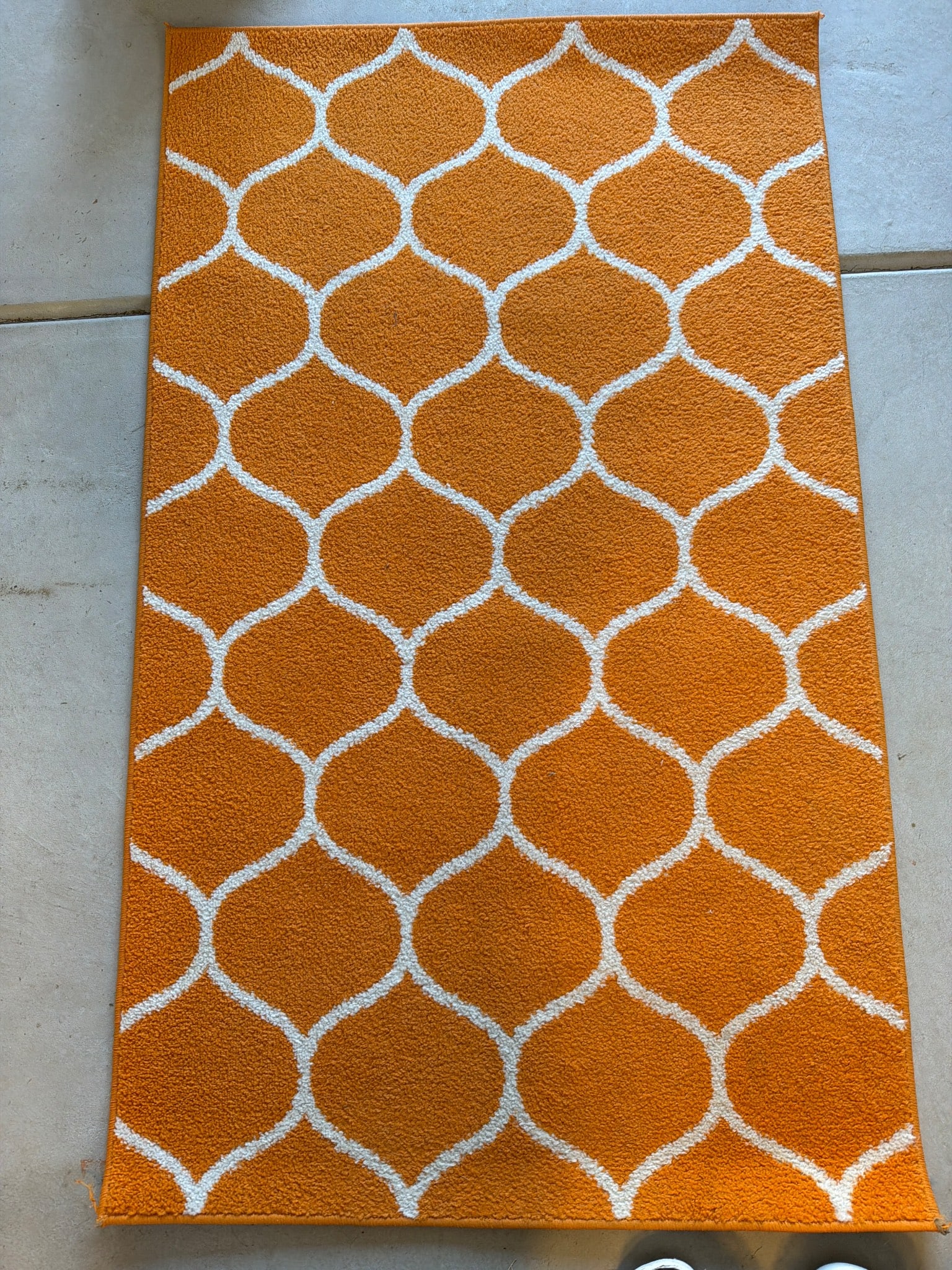 Orange and White Patterned Rug with Lattice Design: Orange rectangular rug featuring a white lattice pattern. It is suitable for various indoor uses. The material is a soft, woven fabric designed for practical home use. Approximate dimensions: 60 inche