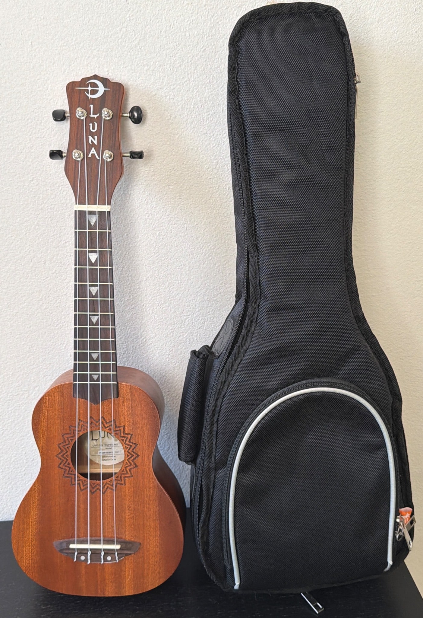Luna Soprano Ukulele with Carrying Case: Luna soprano ukulele, crafted from wood with decorative etching on the body. Model UKE VM Soprano with serial number WSM1609F02.227, made in China. Comes with a black fabric carrying case featuring a