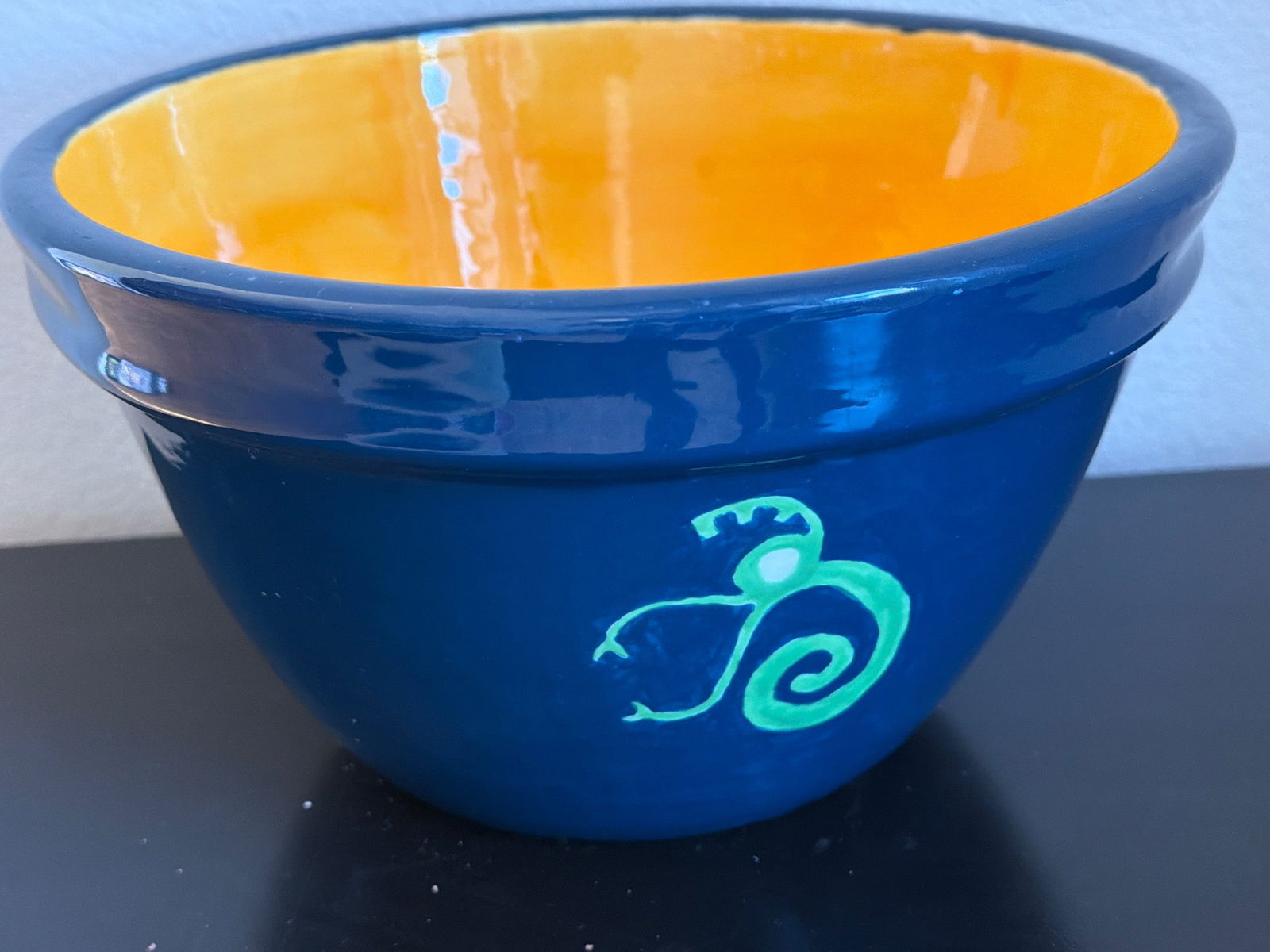 Handmade Ceramic Bowl with Blue Exterior and Orange Interior: Handmade ceramic bowl featuring a vibrant blue exterior with hand-painted green decorative details and a contrasting bright orange interior. The bowl appears to be glazed for durability and shine. Sui