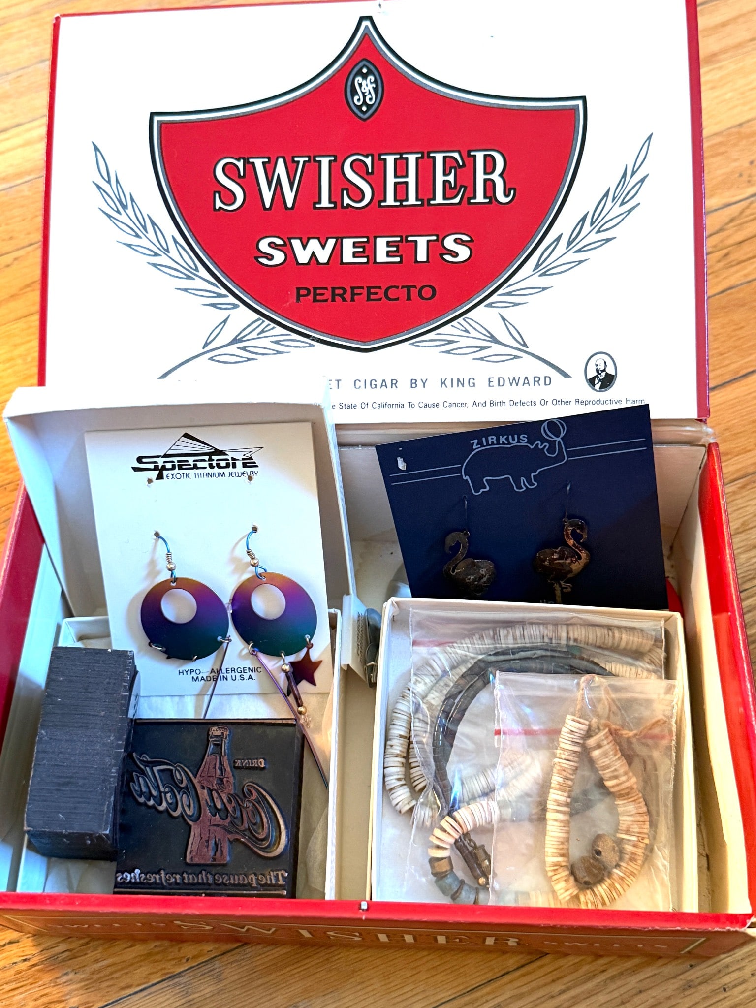 Jewelry and Accessories with Swisher Sweets Box: Jewelry and accessories, including two pairs of earrings, a beaded necklace, a bracelet, and a rectangular decorative item. The pieces appear to incorporate materials such as beads, metals, and other