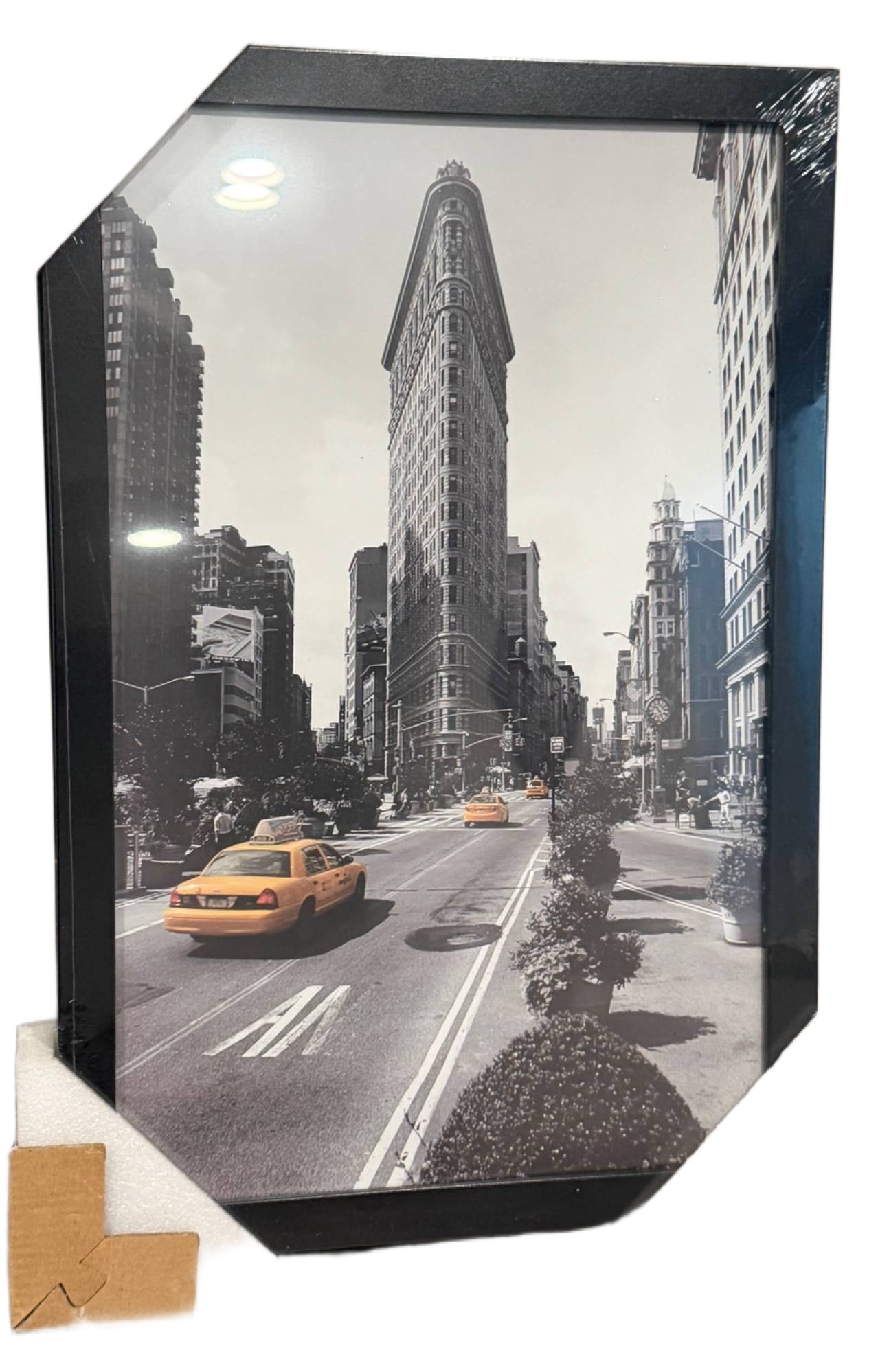 Framed Black-and-White Flatiron Building Print with Yellow Taxis: Framed black-and-white photographic print featuring the iconic Flatiron Building in New York City, with pops of yellow from taxis on the street for a unique contrast. Frame is black with protective