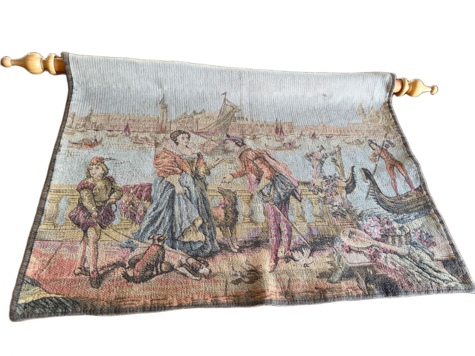 Woven Tapestry Wall Hanging With Wooden Rods: Woven tapestry wall hanging depicting a historical or classical scene. Includes wooden rods at both ends for mounting or display. The piece is colorful and detailed, showcasing a variety of figures