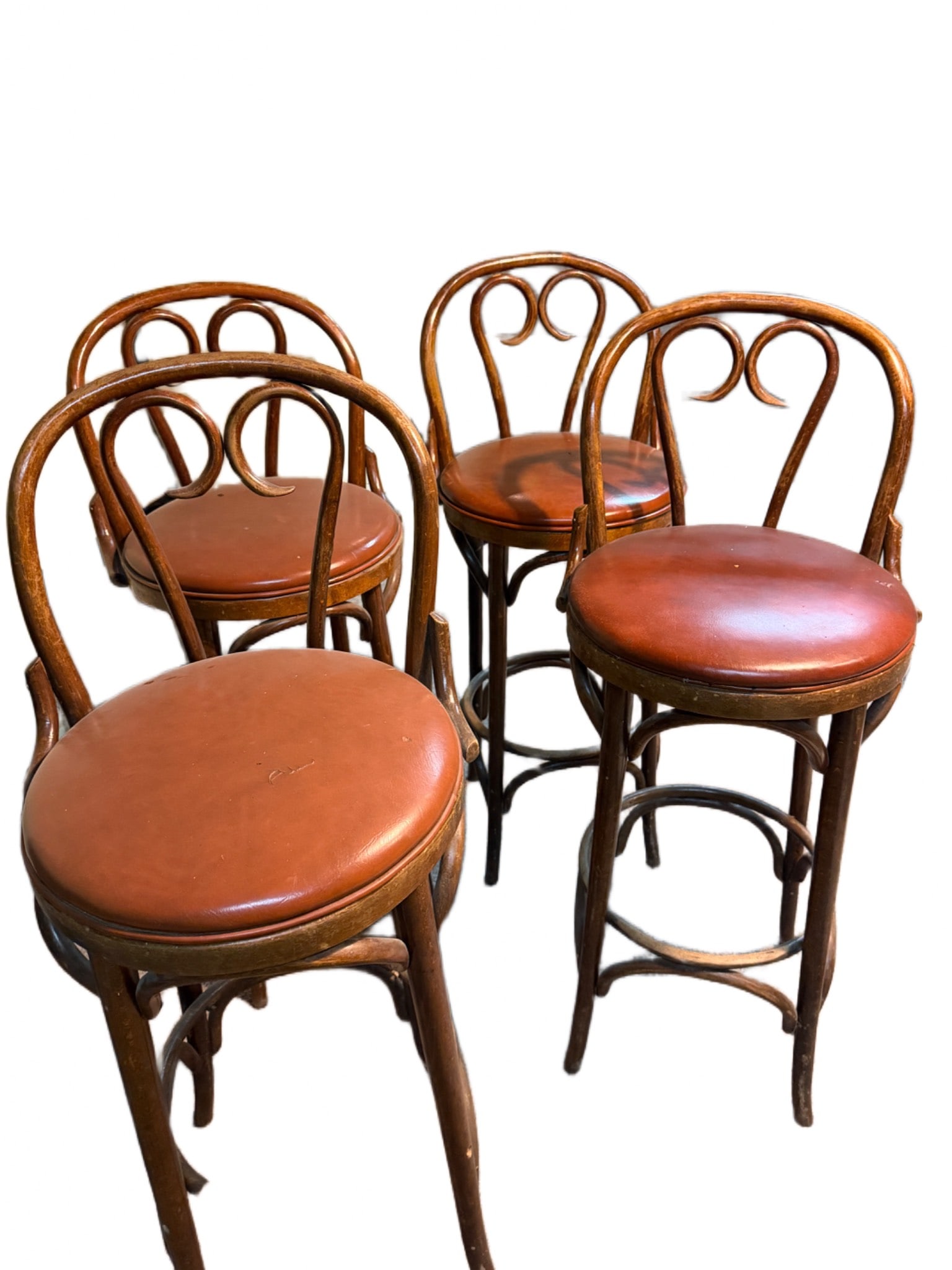 Four Bentwood Bar Stools with Leather Seats: Four bentwood bar stools with rounded backs and leather upholstered seats. The stools feature footrests and a classic design with curved detailing. The leather seats display minor wear, consistent wit