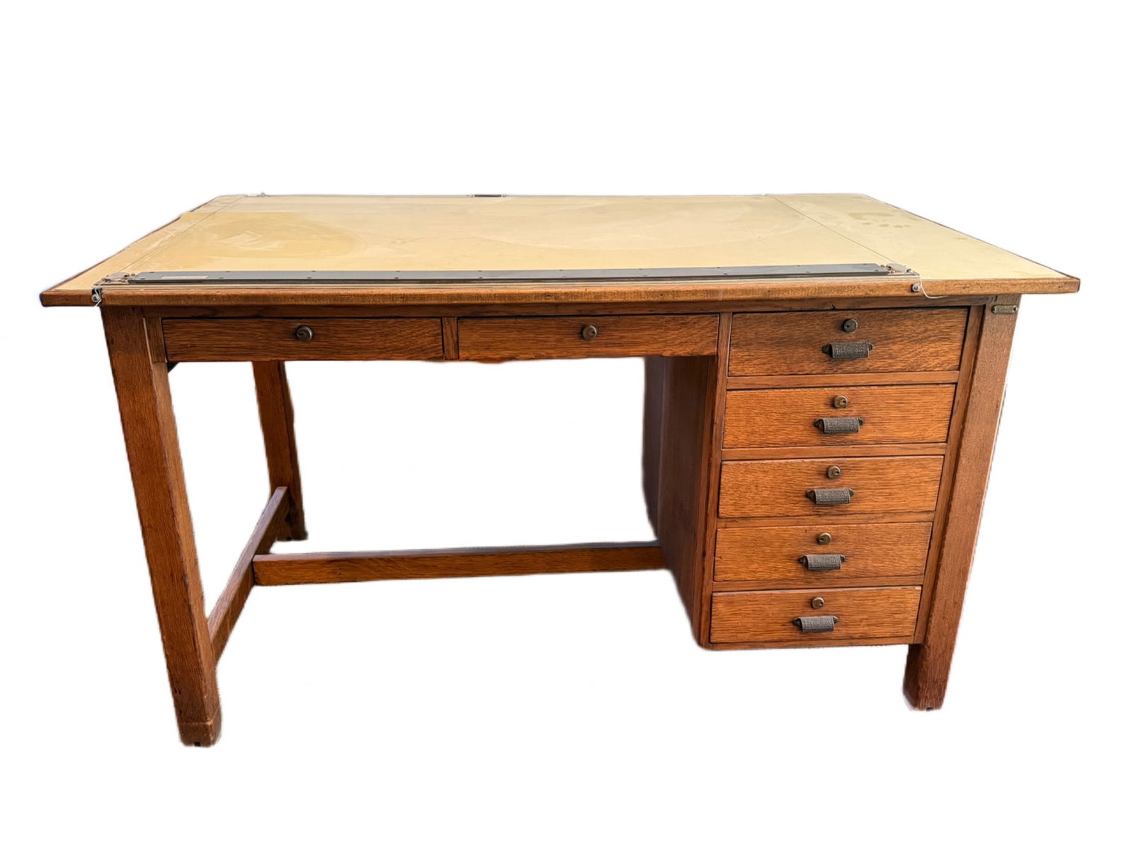 Wooden Drafting Table and Storage: Wooden drafting table, featuring a tan drafting board secured with metal hardware. Includes five side drawers with metal pulls for storage and one central drawer beneath the tabletop. The table measur