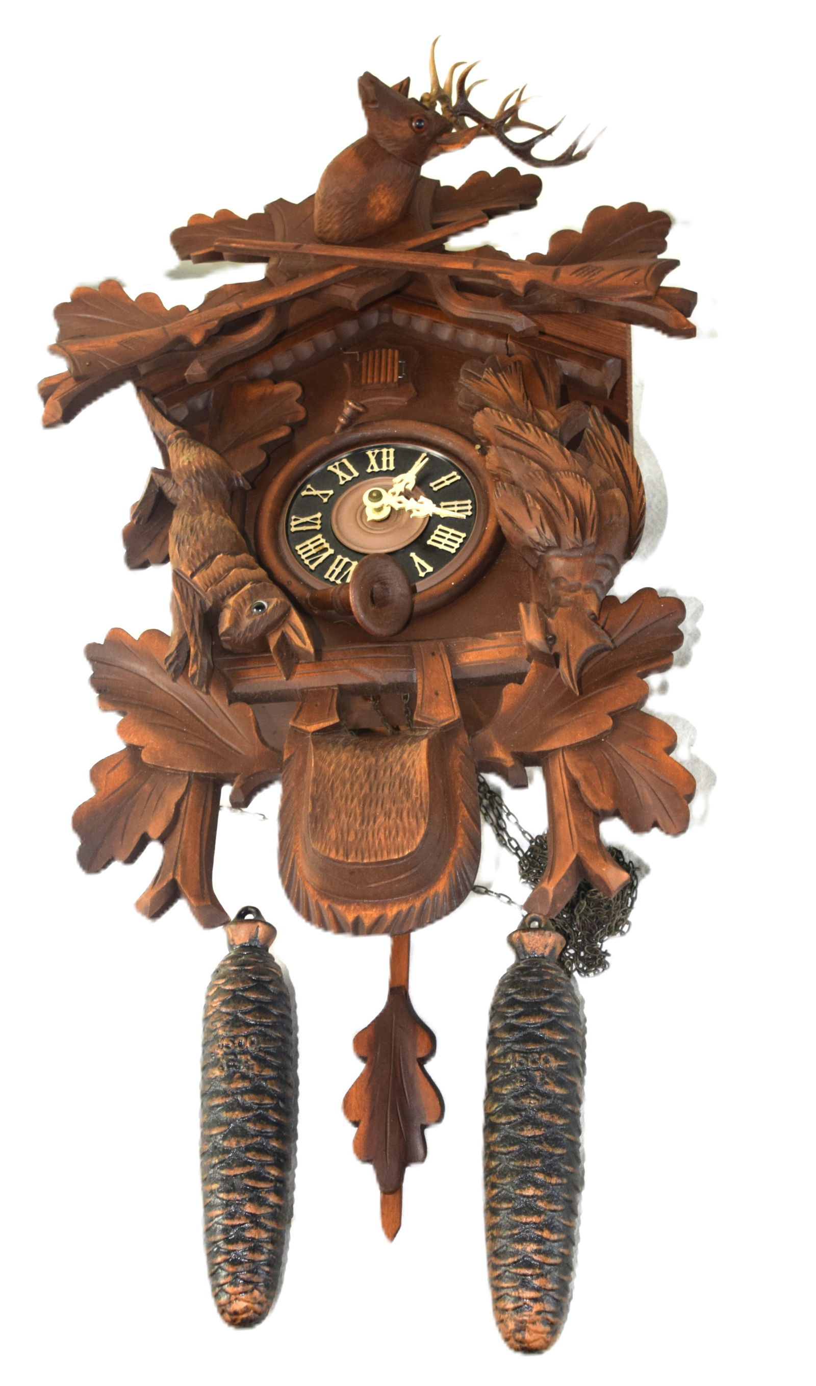 German Cuckoo Clock: German antique Black Forest cuckoo clock with carved game crest, other carved game, Roman numeral dial with pendulum and pine cone design weights. Dimension: 21" H