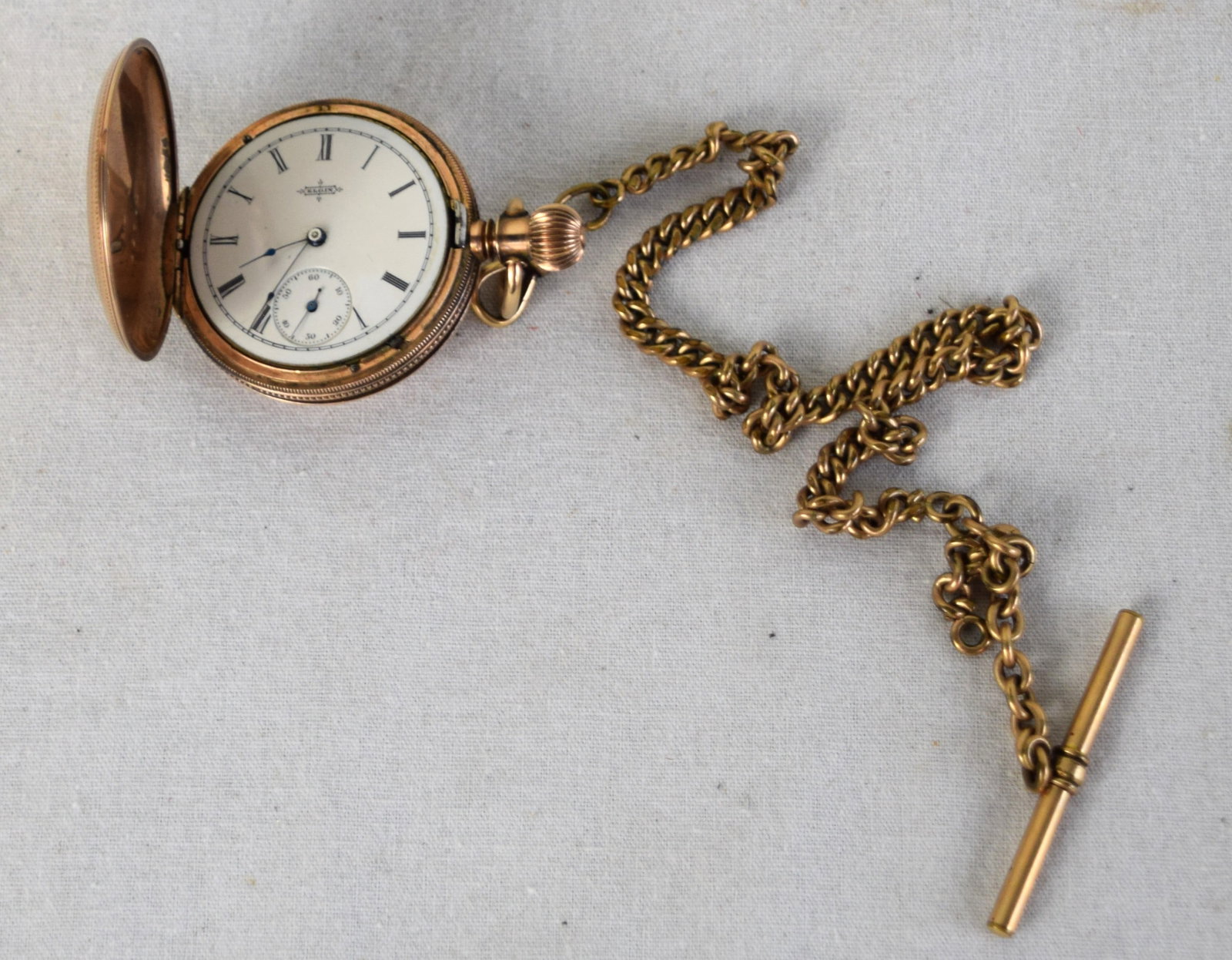 Gold filled Elgin Pocket Watch: Gold filled lady's pocket watch, marked Elgin, with a Roman numeral dial and embossed on front and back side of case with watch chain, serial number 19740.