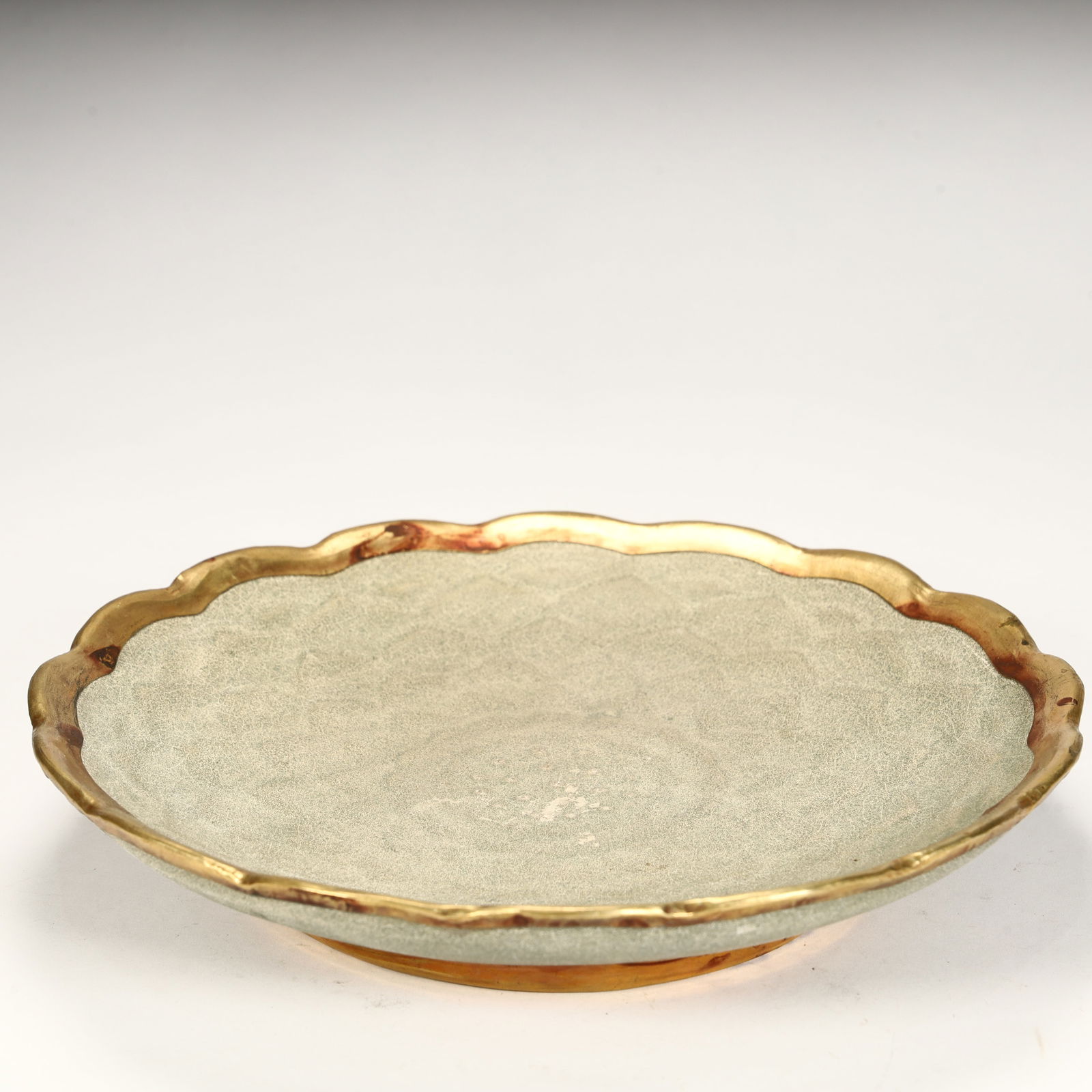 A piece of celadon porcelain, with a natural opening, a flower mouth shape, gilded edges of the: The celadon porcelain, the opening is natural, the flower mouth is shaped, the mouth edge is gilded, and the plate is simple and elegant, reflecting the simple and elegant aesthetic style of the Song