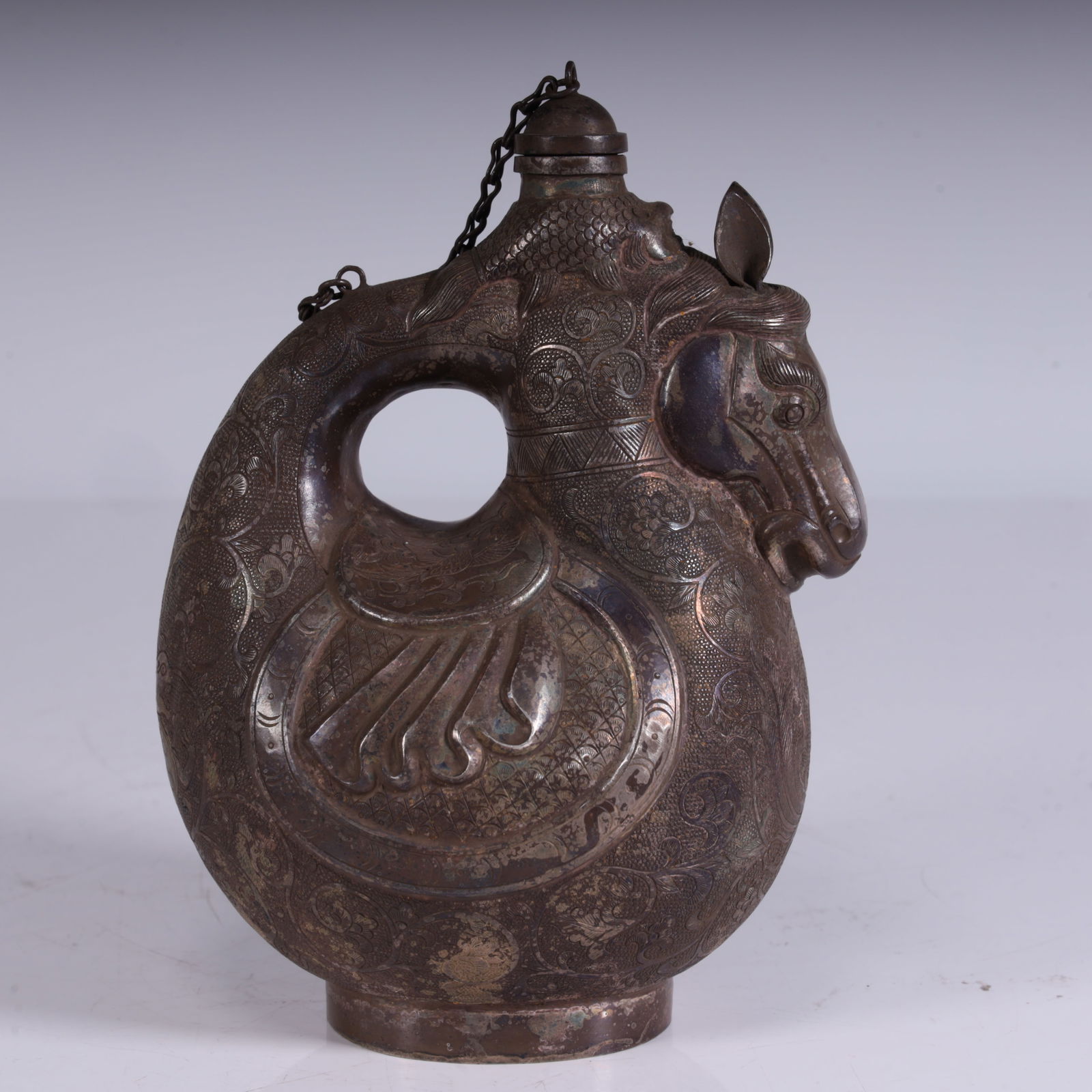 One piece belongs to the silver chisel flower horse head skin pot, made of silver, with an engraved: It belongs to the silver chisel flower horse head skin pot, made of silver, with an engraved pattern on the surface, shaped like a horse head skin bag, with a chain and a lid. It retains the shape cha