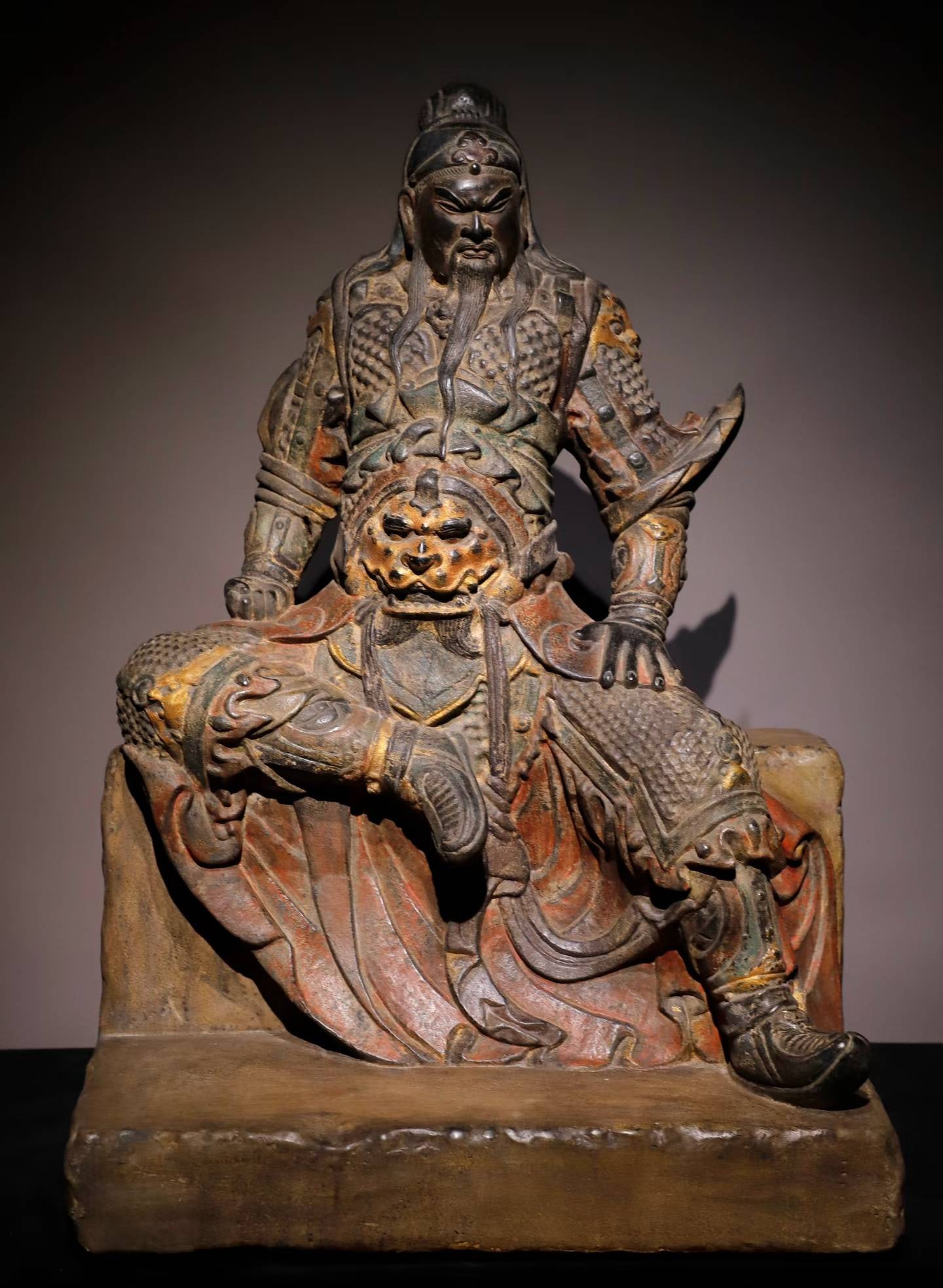 A seated statue of Guan Gong painted in bluestone in the Ming Dynasty: Ming Dynasty bluestone painted Guan Gong seated statue The statue of the God of Wealth has a majestic demeanor, dressed in armor, smooth clothing patterns, and simple colors, showing the majesty of th
