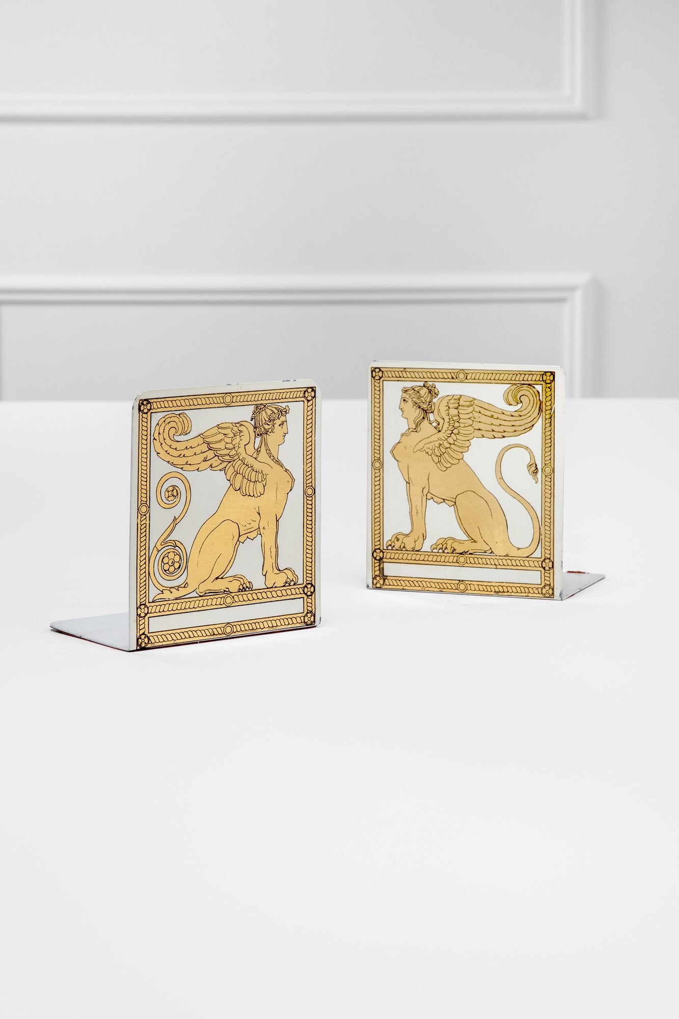 Piero Fornasetti, Coppia di fermalibri mod. Sfingi: Coppia di fermalibri mod. Sfingi Metallo serigrafato. Prod. Fornasetti, 1950 ca. Marchio del produttore sulla fodera sotto la base. cm 15x10x13 LITERATURE: Mariuccia Casadio, Barnaba Fornasetti, Forna