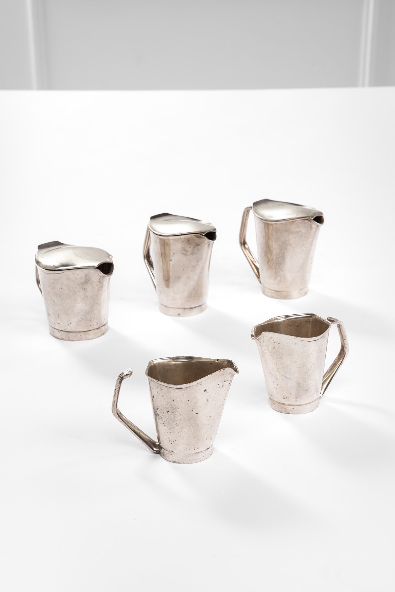 Wilhelm Wagenfeld. Set di tre lattiere e due cremiere: Set di tre lattiere e due cremiere Lega di metallo. Prod. WMF, 1950 ca. Marchio del produttore incusso sotto la base. cm 11x14x8, cm 9,5x12x7, cm 10x16x9