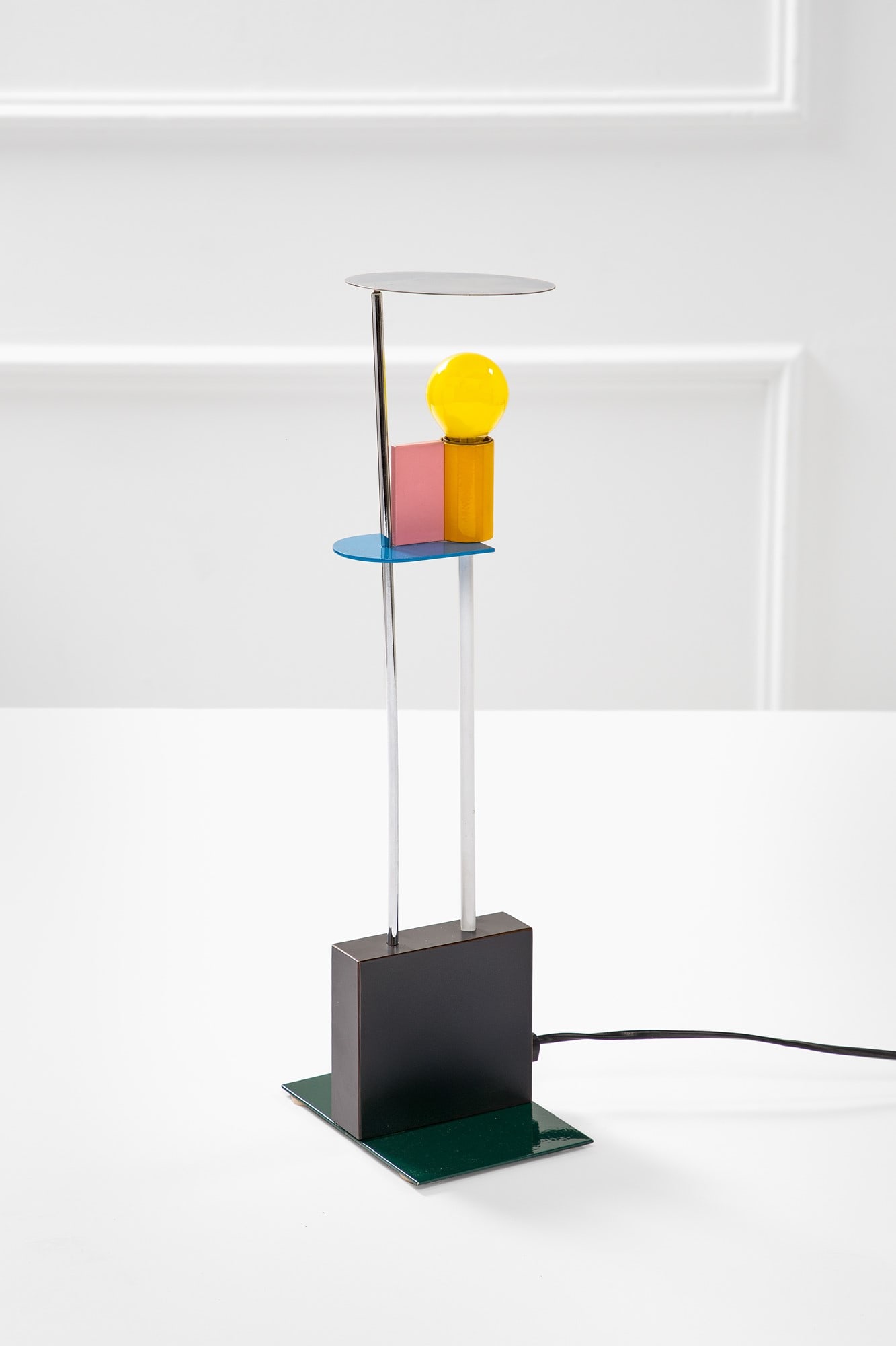 Gerard Taylor. Lampada da tavolo mod. Piccadilly: Lampada da tavolo mod. Piccadilly Laminato plastico, metallo smaltato e cromato. Prod. Memphis, 1982 ca. cm 48x15x11 Literature: Catalogo di produzione Memphis 1982.
