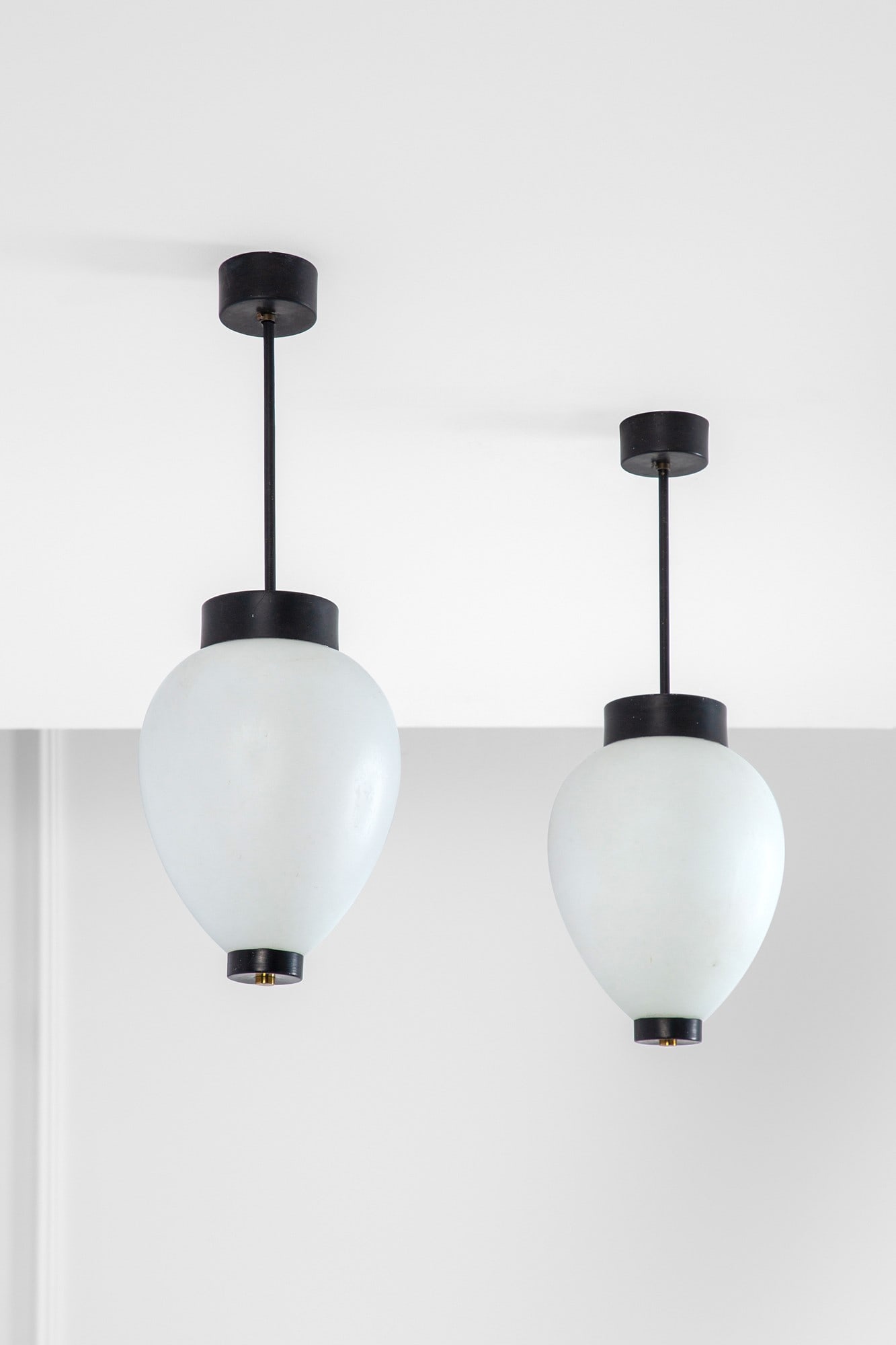 Stilnovo. Due lampade a sospensione: Due lampade a sospensione Metallo verniciato, ottone lucido, vetro satinato. Prod. Stilnovo, 1950 ca. Etichetta del produttore. h cm 60, diam. cm 20