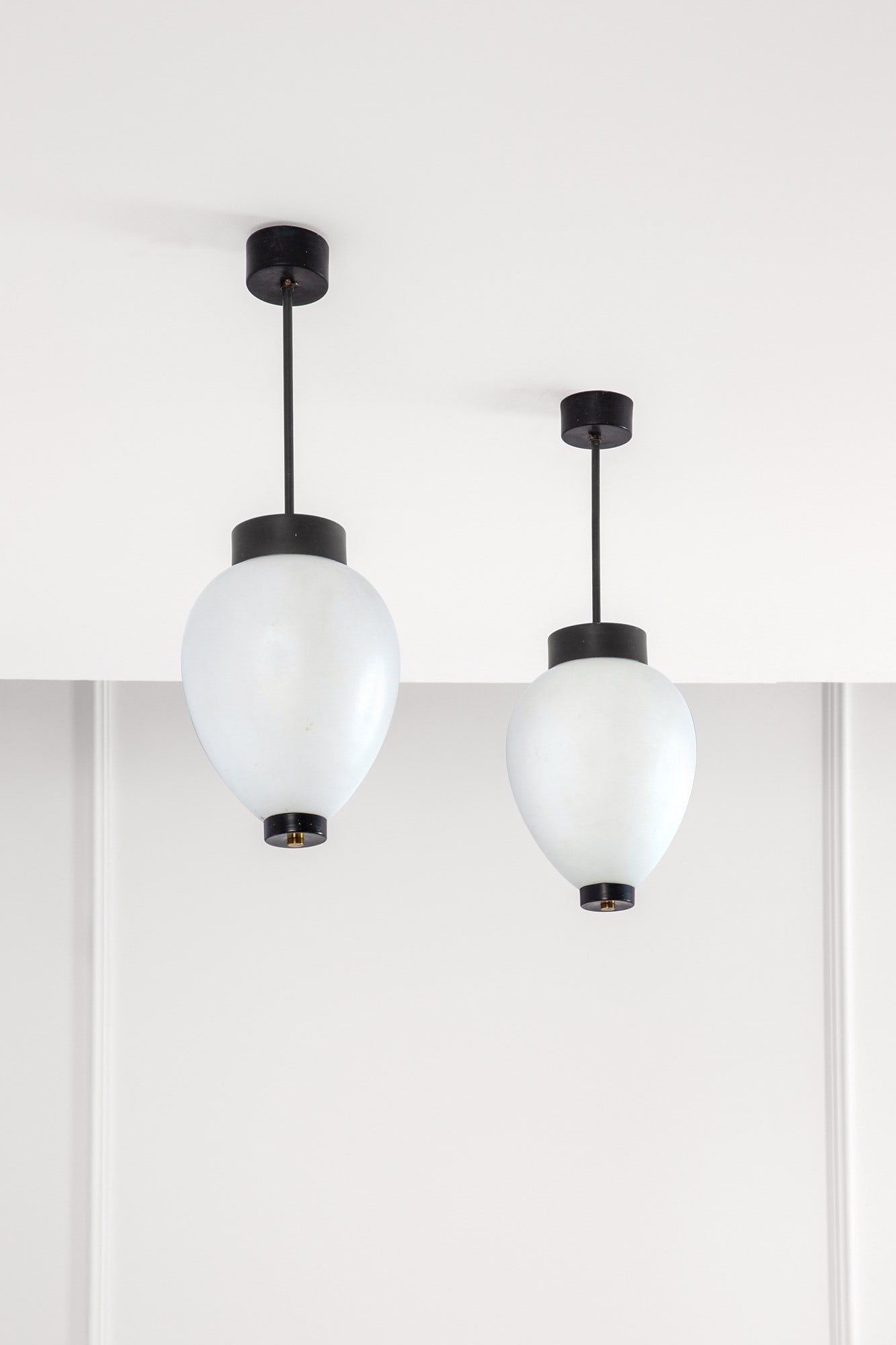 Stilnovo. Due lampade a sospensione: Due lampade a sospensione Metallo verniciato, ottone lucido, vetro satinato. Prod. Stilnovo, 1950 ca. Etichetta del produttore. h cm 60, diam. cm 20