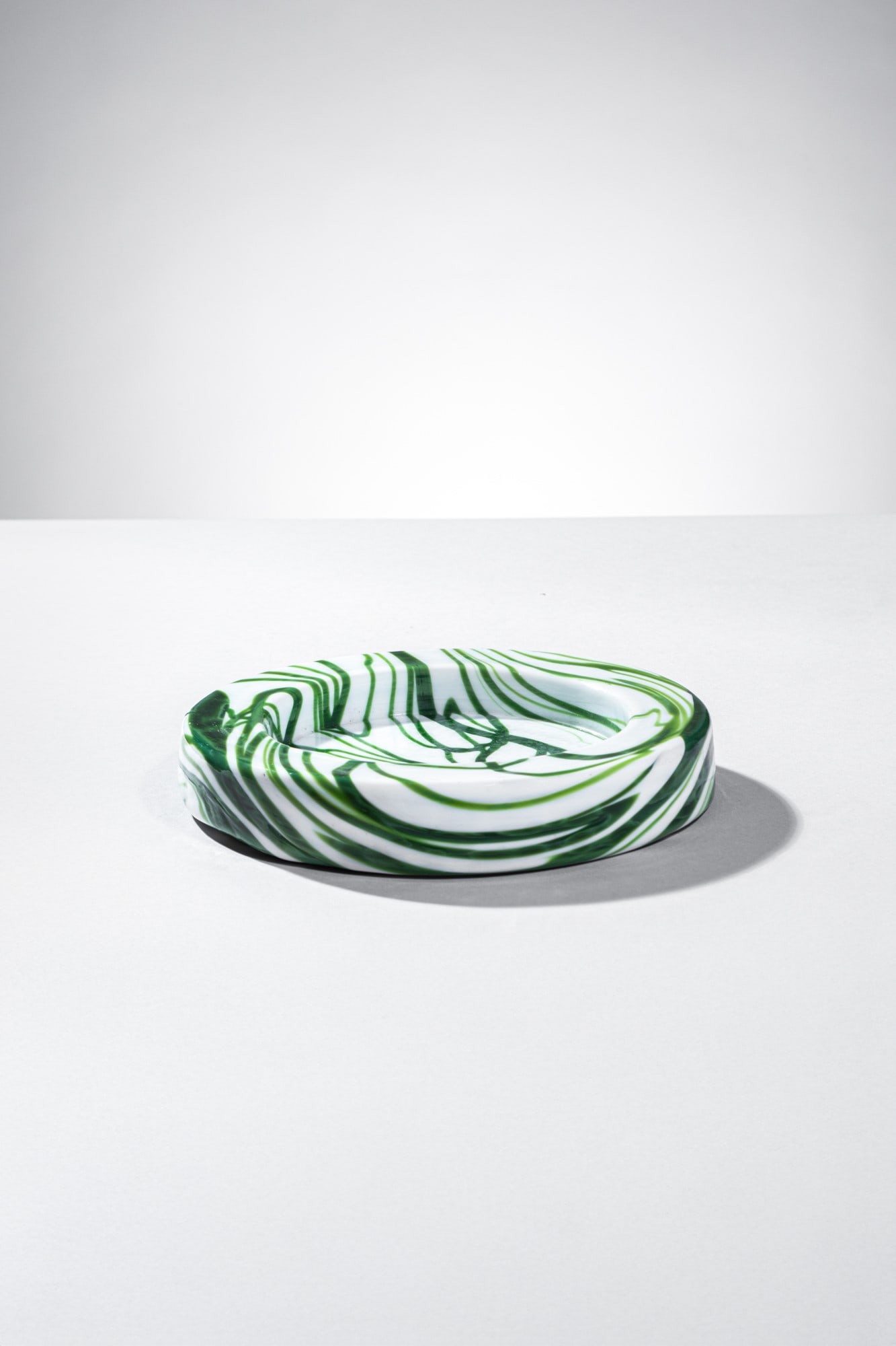 Sergio Asti. Svuotatasche della serie Demodé: Svuotatasche della serie Demodé Vetro soffiato lattimo con inclusioni in vetro verde. Venini, 1950 ca. Firma incisa a punta Venini Italia. h cm 2, diam. cm 18 Bibiliografia: F. De Boni (a cura di), I