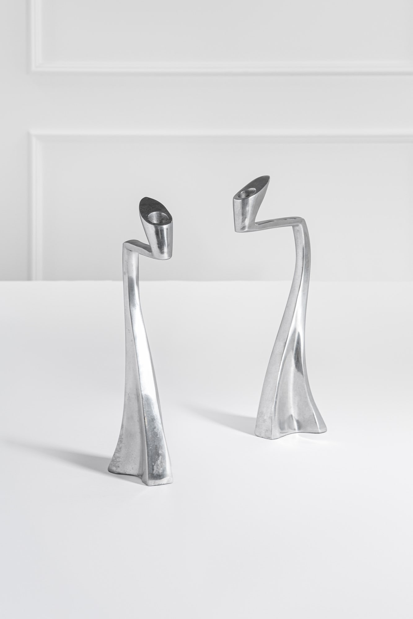 Matthew Hilton, nello stile di. Due candelieri: Due candelieri Fusione di alluminio lucido. 1990 ca. cm 35x9x14