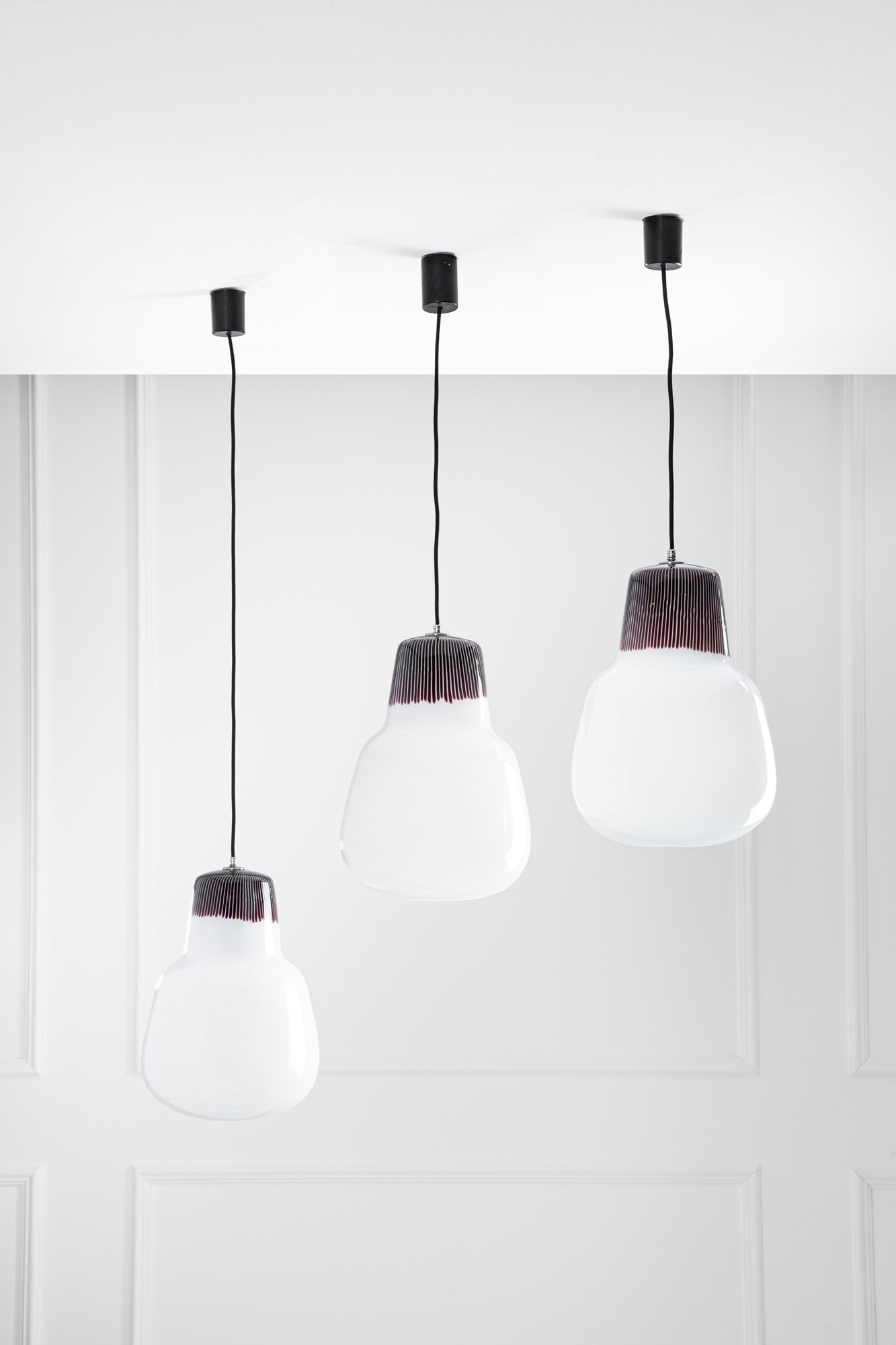 Massimo Vignelli. Tre lampade a sospensione mod. 4037: Tre lampade a sospensione mod. 4037Vetro opalino con tratto superiore tronco-conico a canne verticali ametista scuro.Prod. Venini, 1954-1955.h variabile, diffusore h cm 40, diam. cm 28BIBLIOGRAFIA: