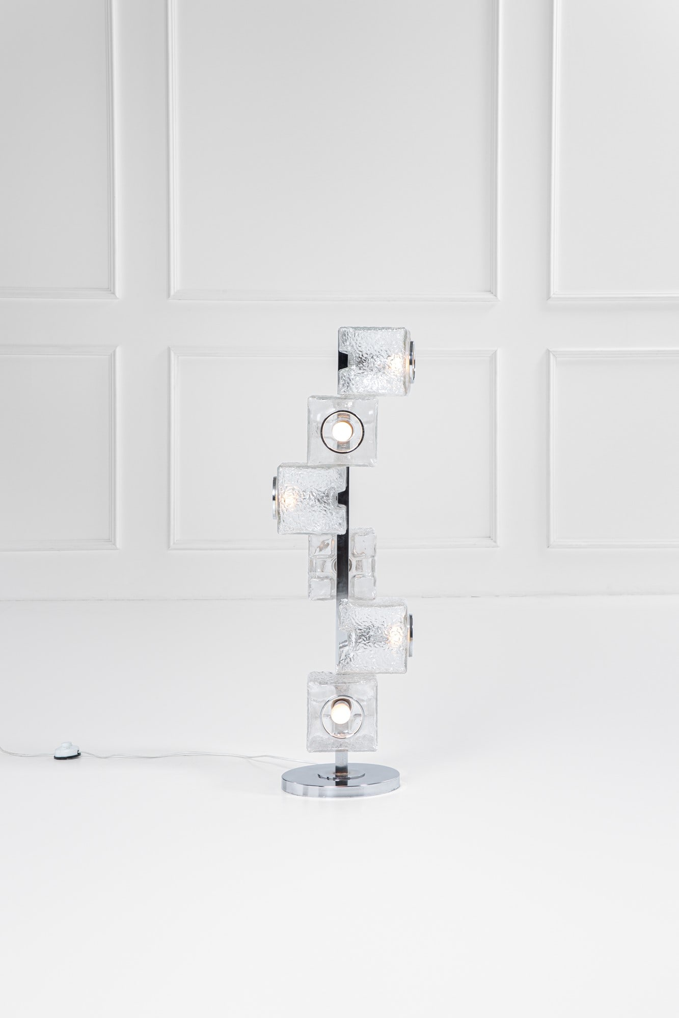 A.V. Mazzega. Lampada da terra: Lampada da terraElementi prismatici in vetro ghiaccio, metallo cromato.Prod. Mazzega, 1970 ca.cm 108x32x32