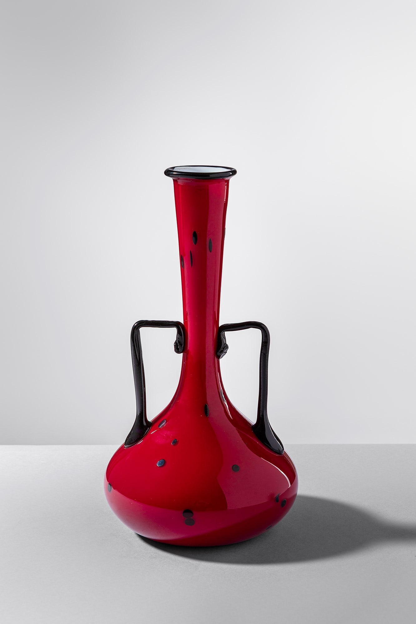 Murano. Vaso biansato: Vaso biansato Vetro soffiato rosso con due anse laterali in vetro nero applicate a caldo, superficie decorata con puntini neri. Murano, 1920 ca. h cm 24, larg. cm 13