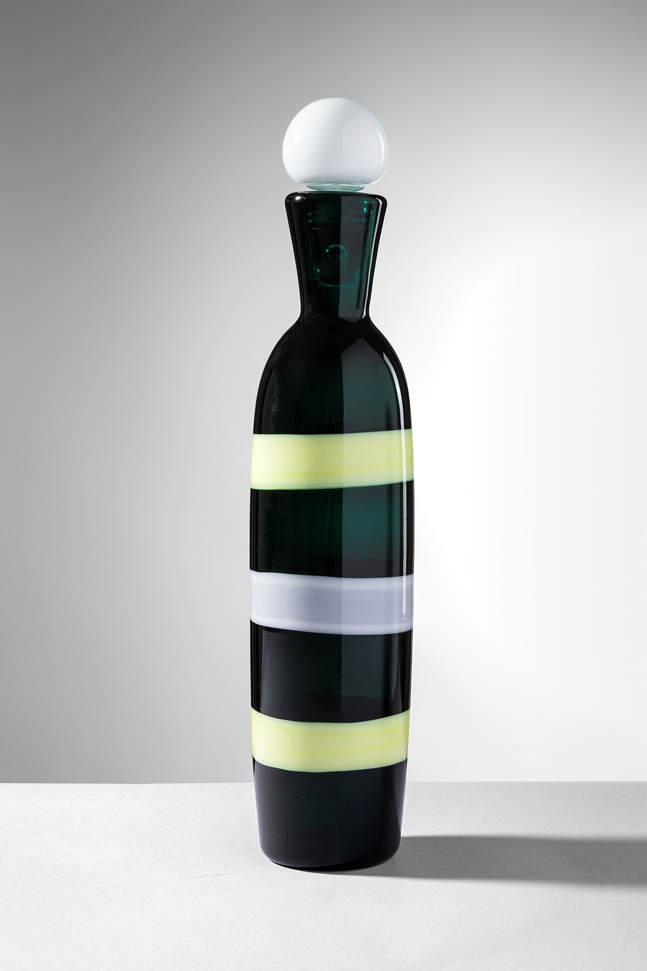 Fulvio Bianconi. Bottiglia a fasce orizzontali mod. 4581: Bottiglia a fasce orizzontali mod. 4581 Vetro soffiato verde decorato da fasce orizzontali giallo e lattimo. Venini, 1953-56. Firma all'acido Venini Murano Italia. h cm 41, diam. cm 7 Bibliografia: Ma