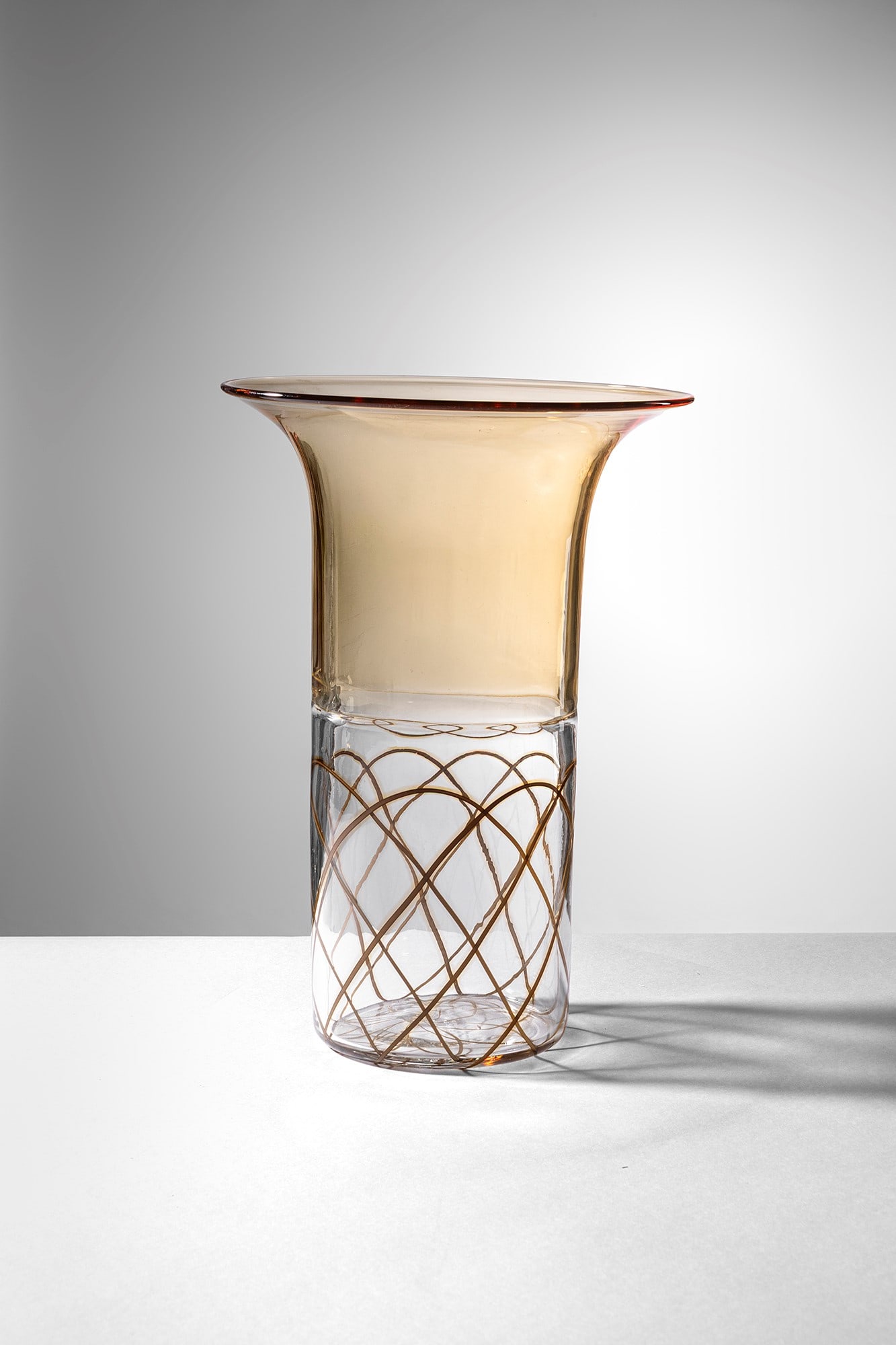 Lino Tagliapietra. Vaso ad incalmo: Vaso ad incalmo Vetro soffiato a due corpi incalmati, il superiore di color topazio, l’inferiore di cristallo con reticolo di fili marrone. Effetre International, 1986. Firma incisa a punta Lino