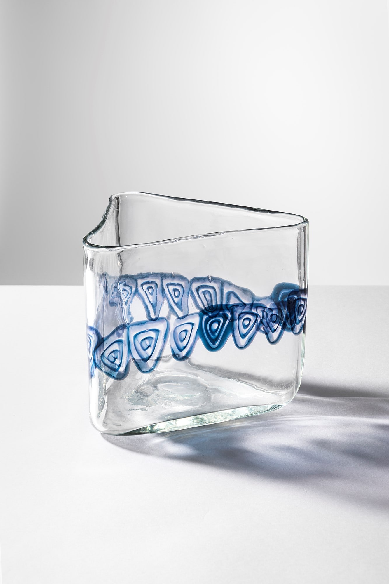 Gianmaria Potenza. Vaso della serie S/196 d: Vaso della serie S/196 d Vetro soffiato cristallo a sezione triangolare decorato con murrine blu. La Murrina, 1970 ca. cm 17x20x18 Bibliografia: Catalogo La Murrina.