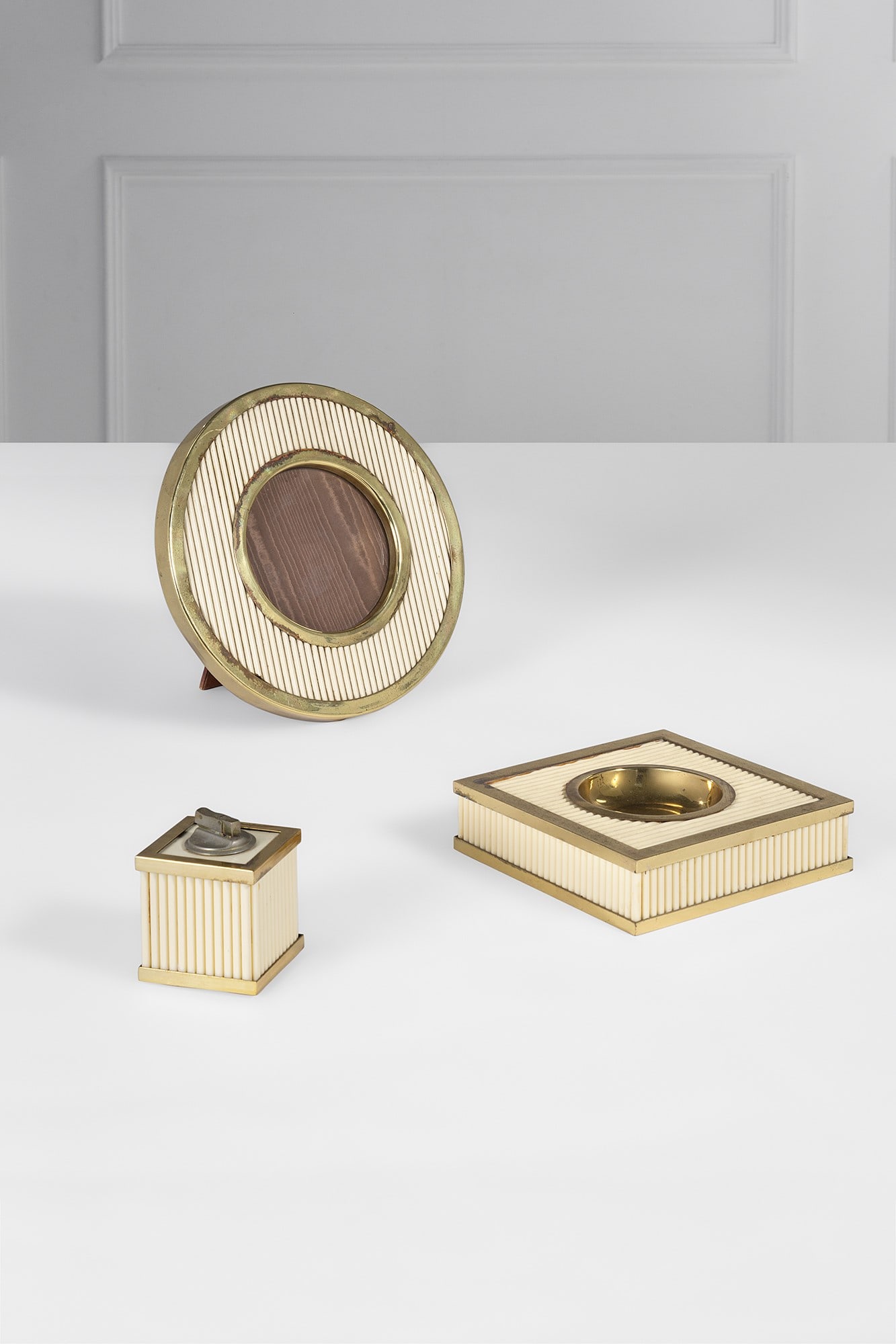 Tommaso Barbi. Set da fumo e cornice portafoto: Set da fumo e cornice portafoto Ottone, resina plastica ad imitazione dell'avorio. 1970 ca. Etichetta dell'atelier. Accendisigari cm 11x8x8; posacenere cm 6x20x20; cornice diam. cm 30