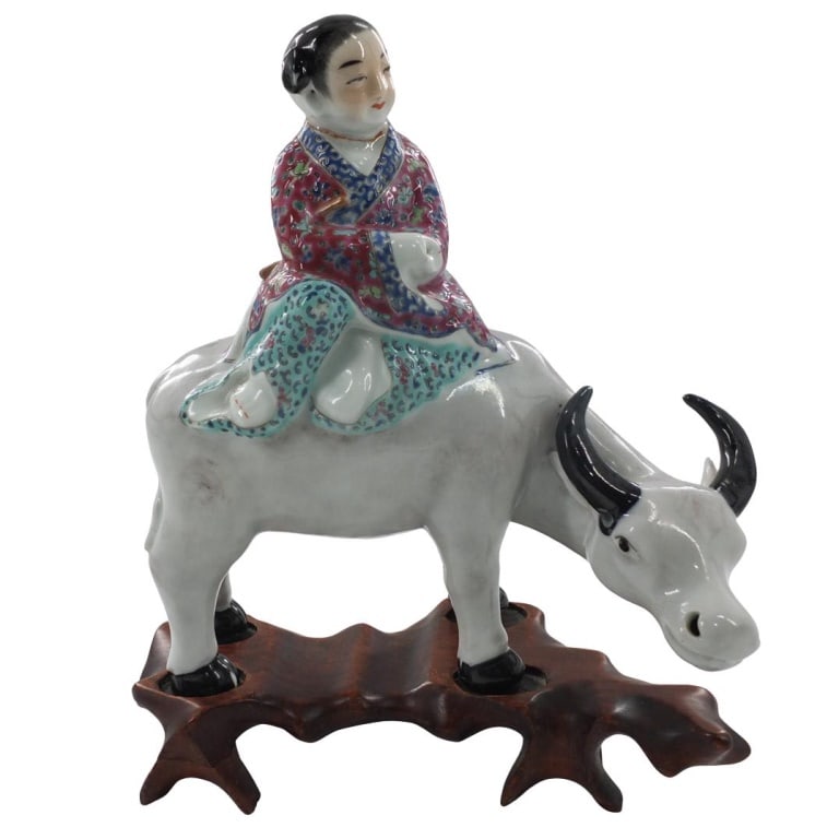 19/20th C. Chinese Porcelain Figurine: 19/20th Century Chinese Famille Rose Porcelain Ox Rider Figurine Presented on a Wooden Base. Unsigned. Figurine measures 8-1/8" x 4" x 7-1/4". Condition: Figurine and stand are in good condition. Esti