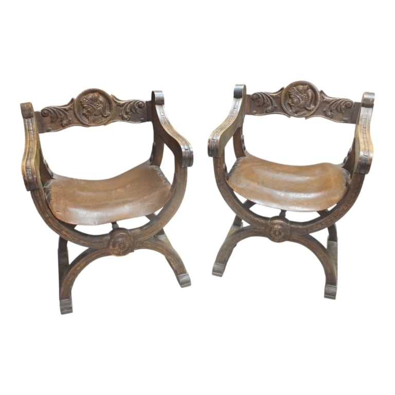 Pair of Italian Savonarola Chairs: Pair of Italian Renaissance Style Carved Wooden Savonarola Chairs with Leather Seat Rest. Measures 31" x 24-1/4", 18" seat height. Condition: Scuffs and scratches to the wood. Leather has some