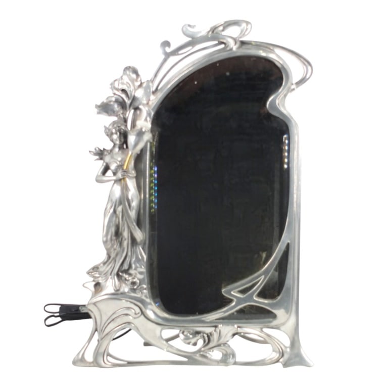 Silvered Art Nouveau Table Mirror: Silvered Art Nouveau Table Mirror with Light. Late 19th Century with a stylized frame with a maiden standing to one side holding a flower form light socket. Unsigned. Measures 24-1/4" H x 17" W.
