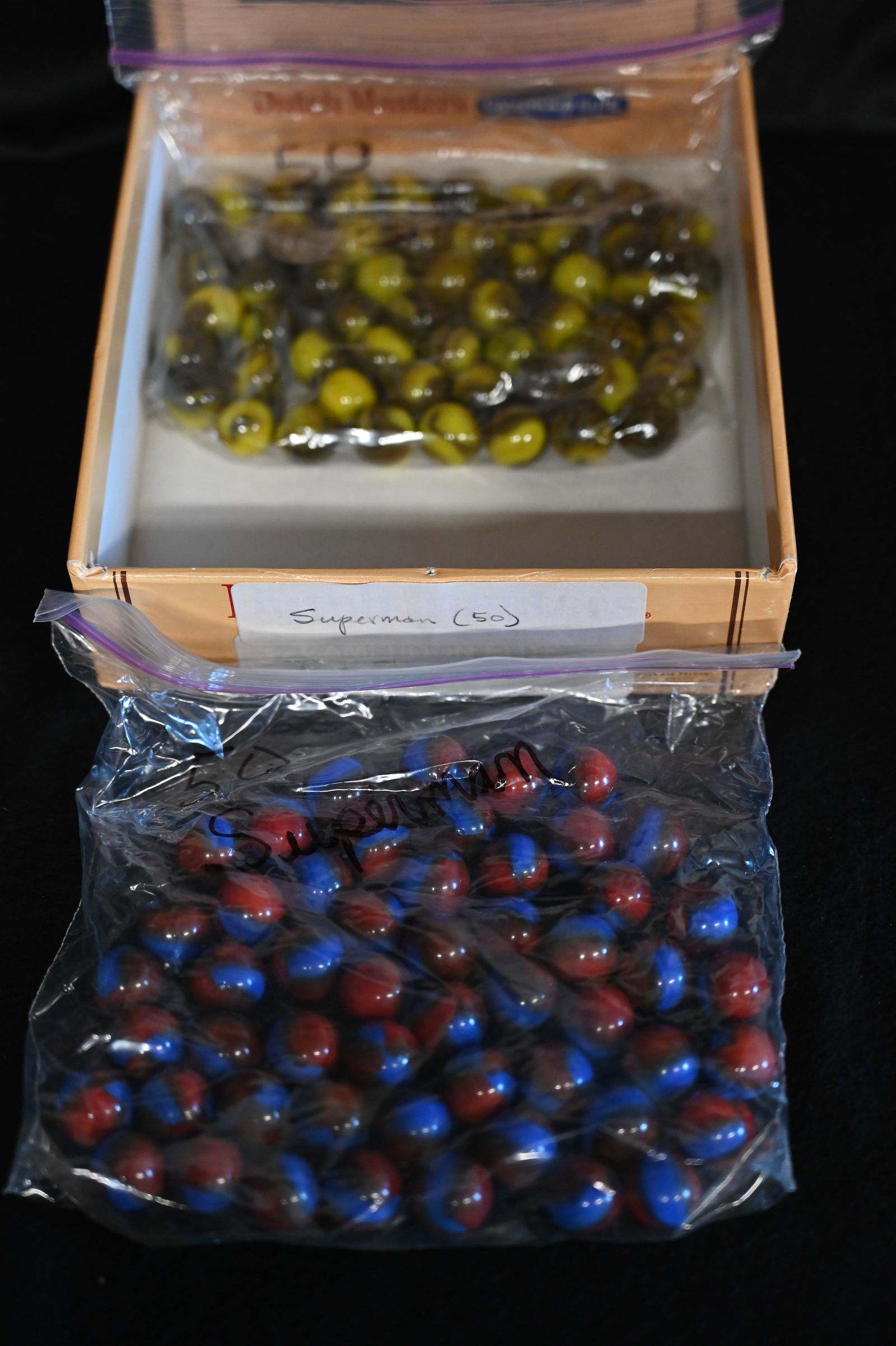 50 Superman Marbles and 50 Tiger Stripes Marbles in a Dutch Masters Cigar Box. The size of the: 50 Superman Marbles and 50 Tiger Stripes Marbles in a Dutch Masters Cigar Box. The size of the marbles is 5/8".