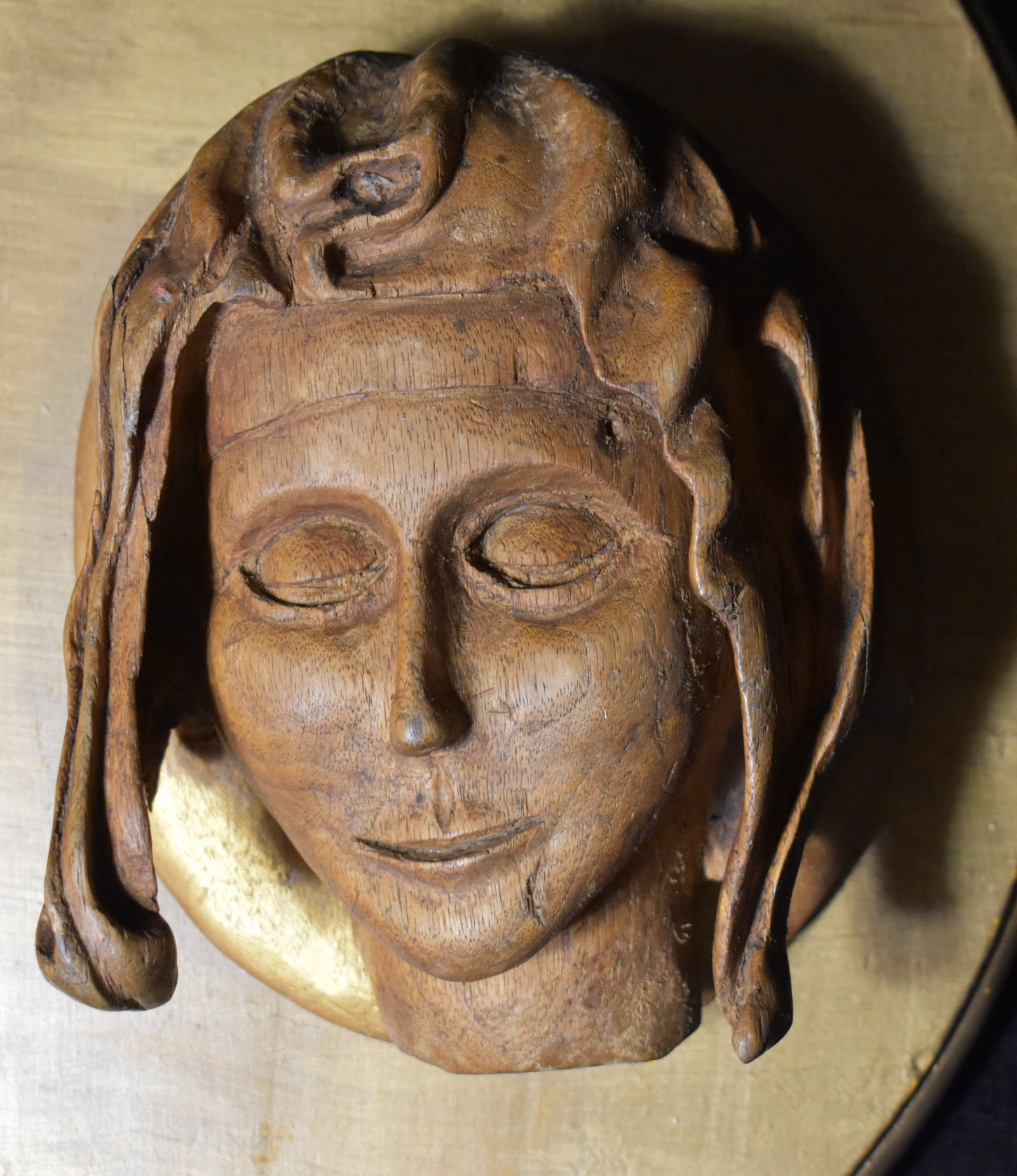 Mid 20th Century Hand Carved Wood Relief Plaque — Stylized Face on Oval Panel: A mid 20th century hand carved wood relief plaque depicting a serene stylized human face with flowing hair mounted on an oval wooden backboard. The carving features smooth rounded contours and a peace