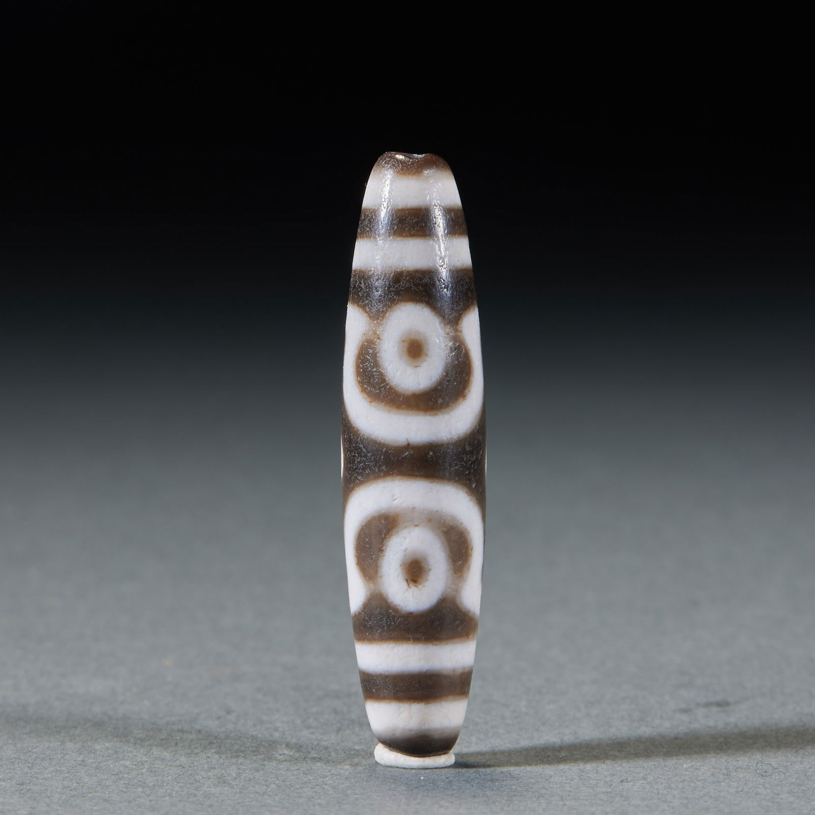 Three-eyed dzi bead: Three-Eyed Dzi Bead, H: 4.8cm, D: 1.2cm, 10g. Passed down or unearthed in the Xizang area, it is a sacred object of Tibetan Buddhism made of nine-eyed stone shale (natural agate), with the black and