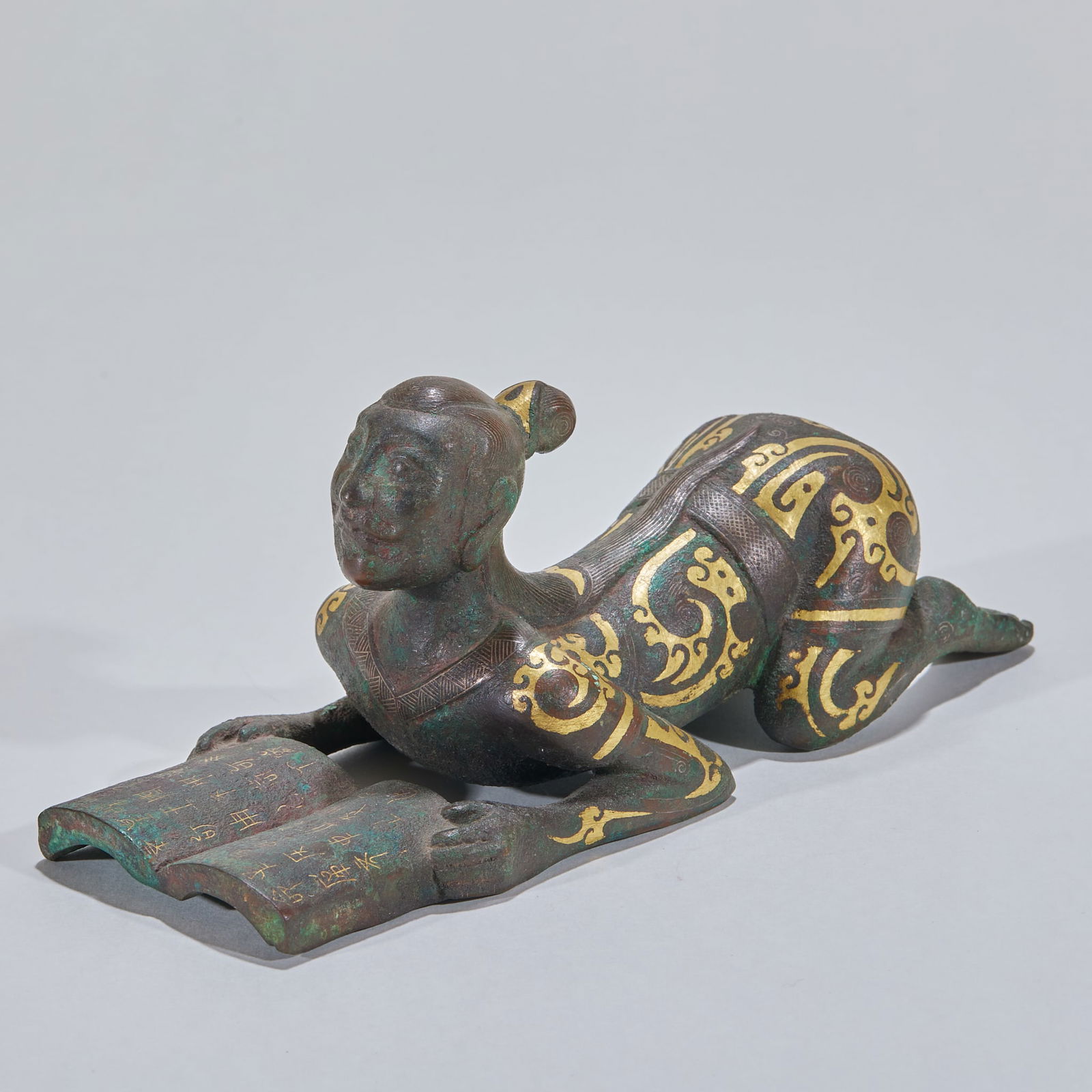 Inlaid Gold and Silver Human Figure Paperweight: Gold and Silver Inlaid Figure Weight. Height 7cm, length 16cm, width 6.5cm. Warring States to Han noble mat weight for pressing mat corners, influenced by Chu culture. Bronze with gold and silver