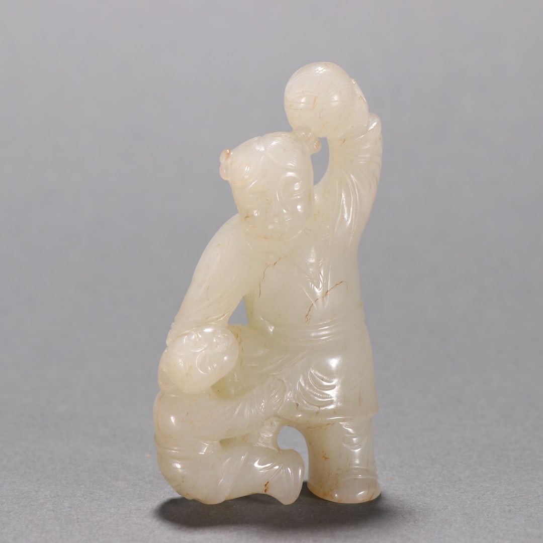 Qing Dynasty Hetian jade figurine of children playing with a ball: Qing Hotan Jade Boy Playing Ball. Height 7.9cm, width 4.3cm, weight 82g. Qing court or scholar’s studio display, a lucky ornament. Hotan white jade with natural reddish-brown infiltration. Round