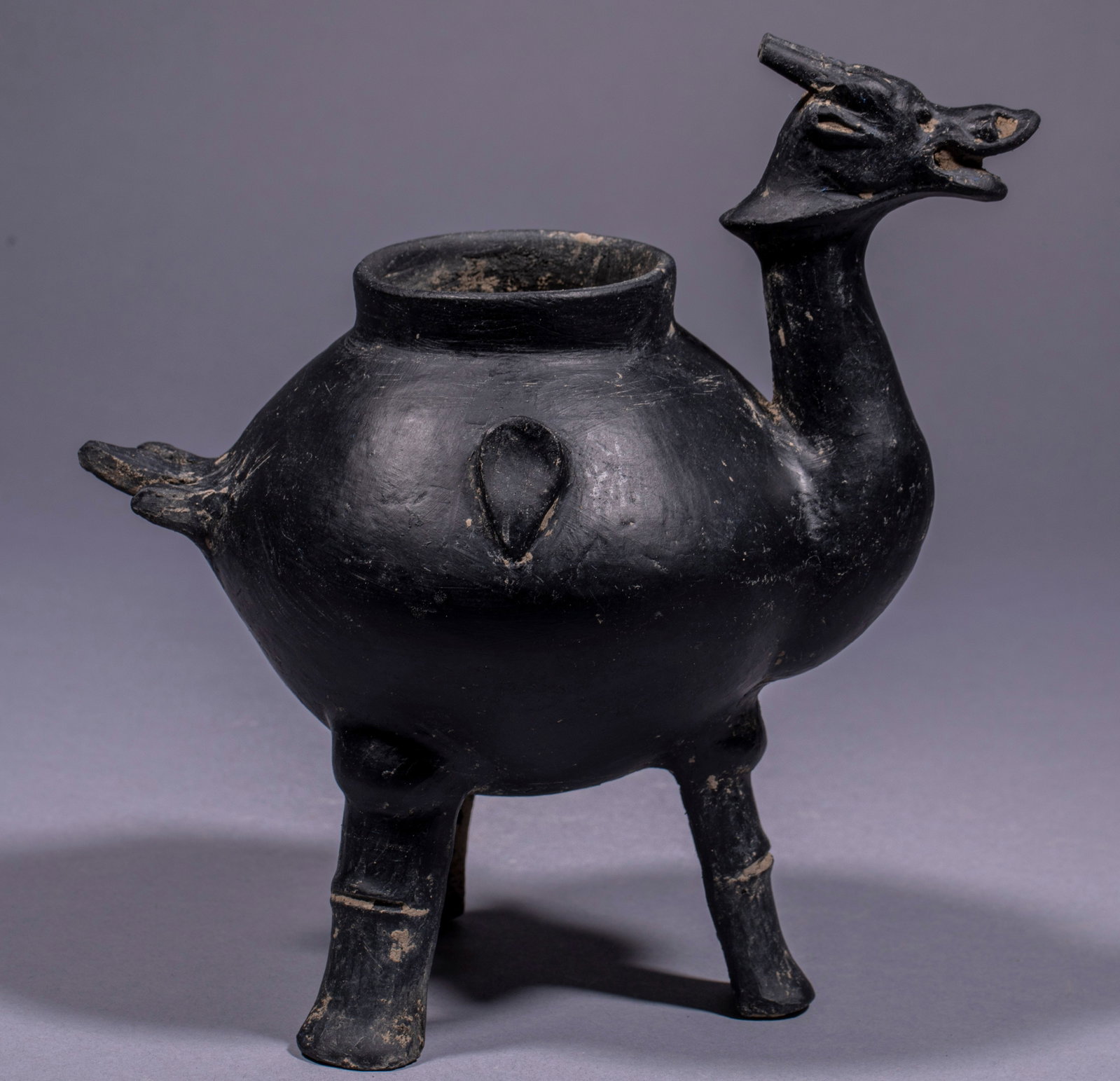 Three-legged animal head pottery pot: Black pottery texture, the body is round and bulging, the mouth is straight neck and round mouth, one side extends out of the animal head, the tail is short, and the bottom is supported by three anima