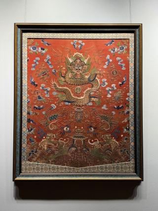 Embroidered dragon pattern fish dragon in Qing dynasty: Framed furnishings, red fabric. The main body weaves and embroiders a dragon with five claws. The dragon body is rich, and auspicious clouds, auspicious beasts, phoenix birds, babao and other