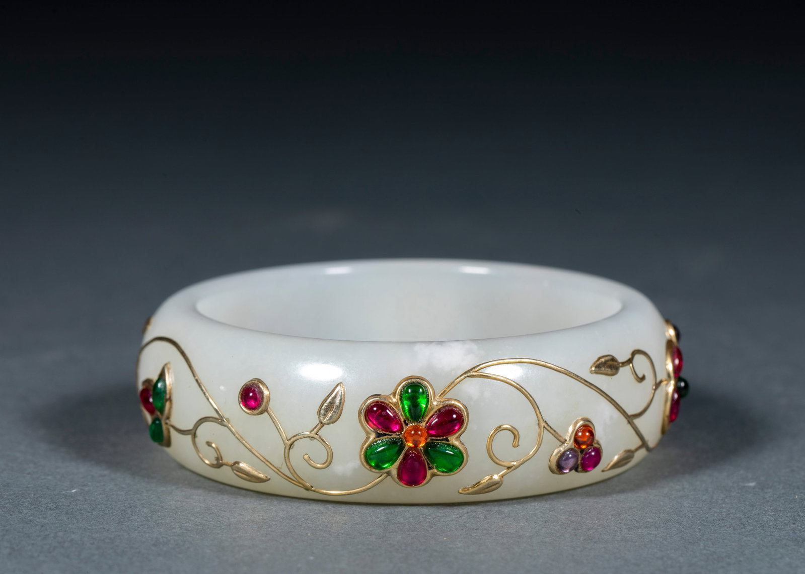 Hetian jade inlaid bracelet: The wide flat bracelet is made of hetian white jade, and its temperature is moist and white. The bracelet body is stamped with gold thread to form the vine outline of the twined flowers, and the flowe