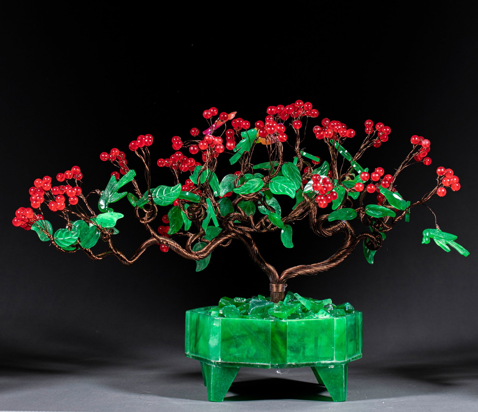 Bonsai with four feet and eight edges, where flowers are like fire and birds offer blessings.: The copper wire is twisted to make the trunk, and the branches bend and stretch. The leaves are jadeite, red beads are used as fruits, and the fruits are clustered. The base is made of jade,