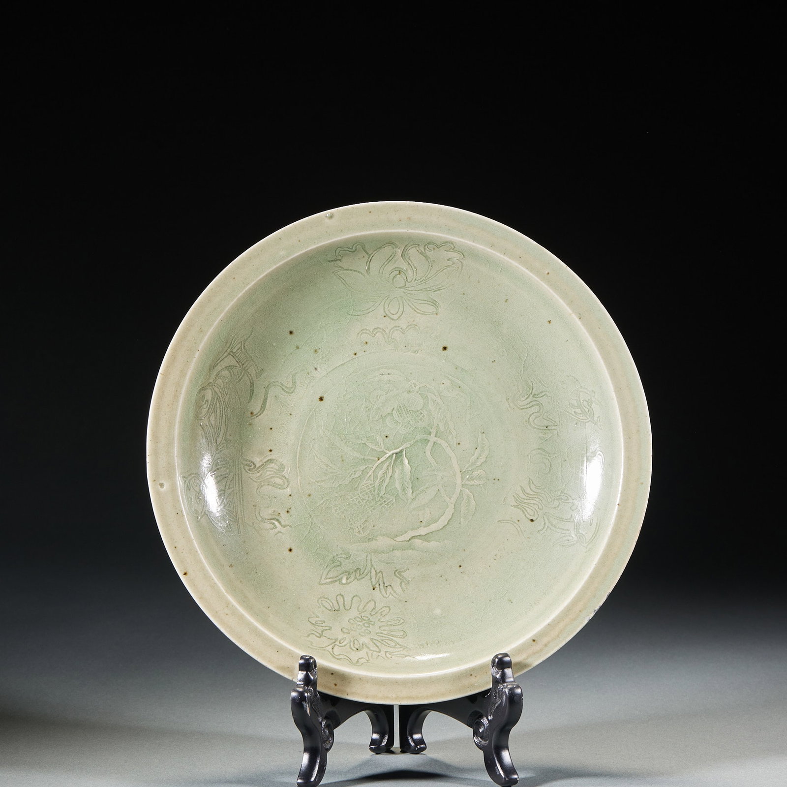 Longquan kiln flower pattern appreciation plate: Open shallow belly plate, full of green glaze. The center of the dish is carved with branches and leaves of Shoutao, and the inner wall of the dish is surrounded with patterns of lotus, chrysanthemum