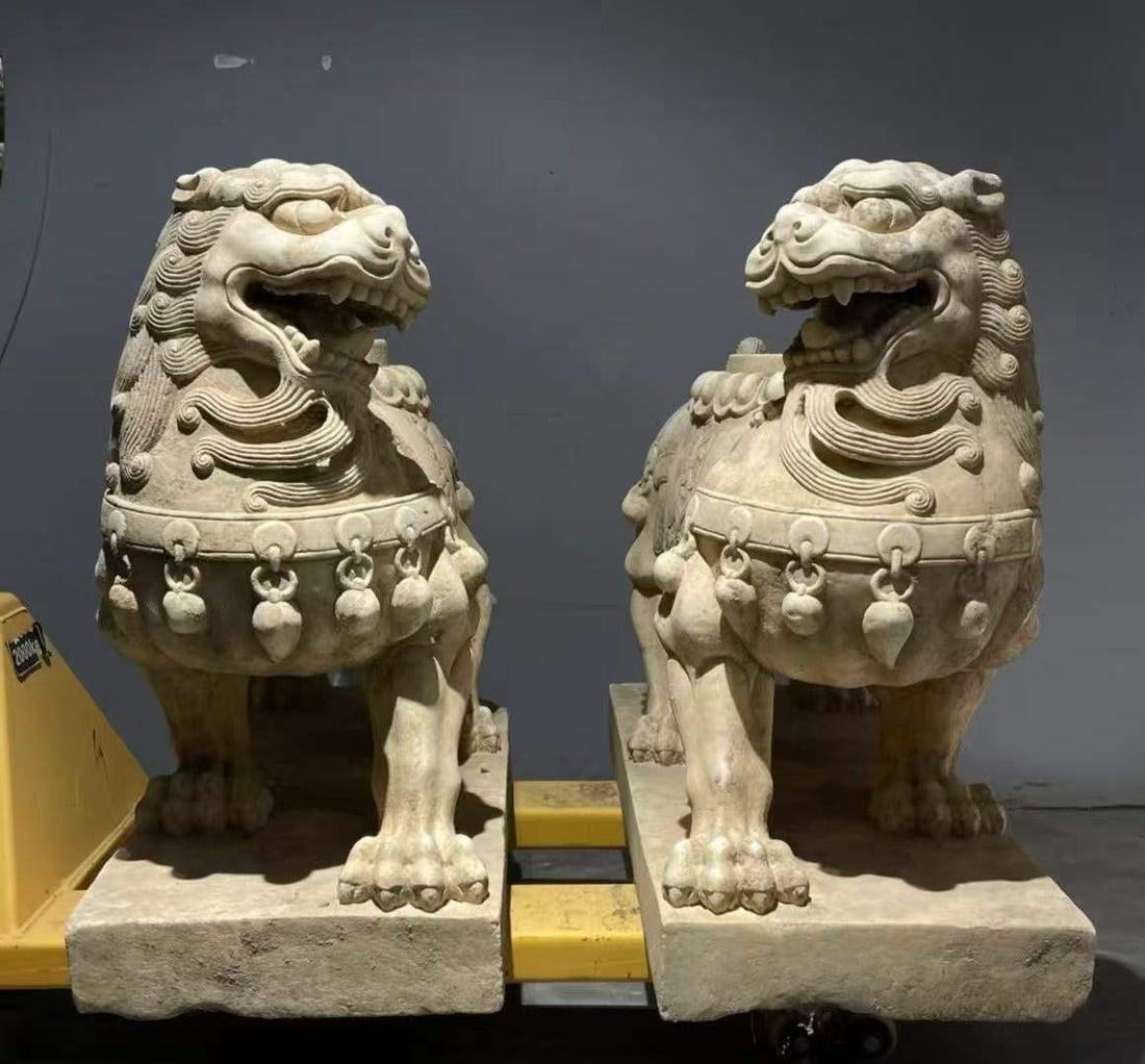 A pair of white marble door lions: White marble, paired stone lions crouching on a square stone seat. The lion's head is high, his mouth is open and his teeth are bared, his mane is curly, he wears bells and round ornaments on his ches