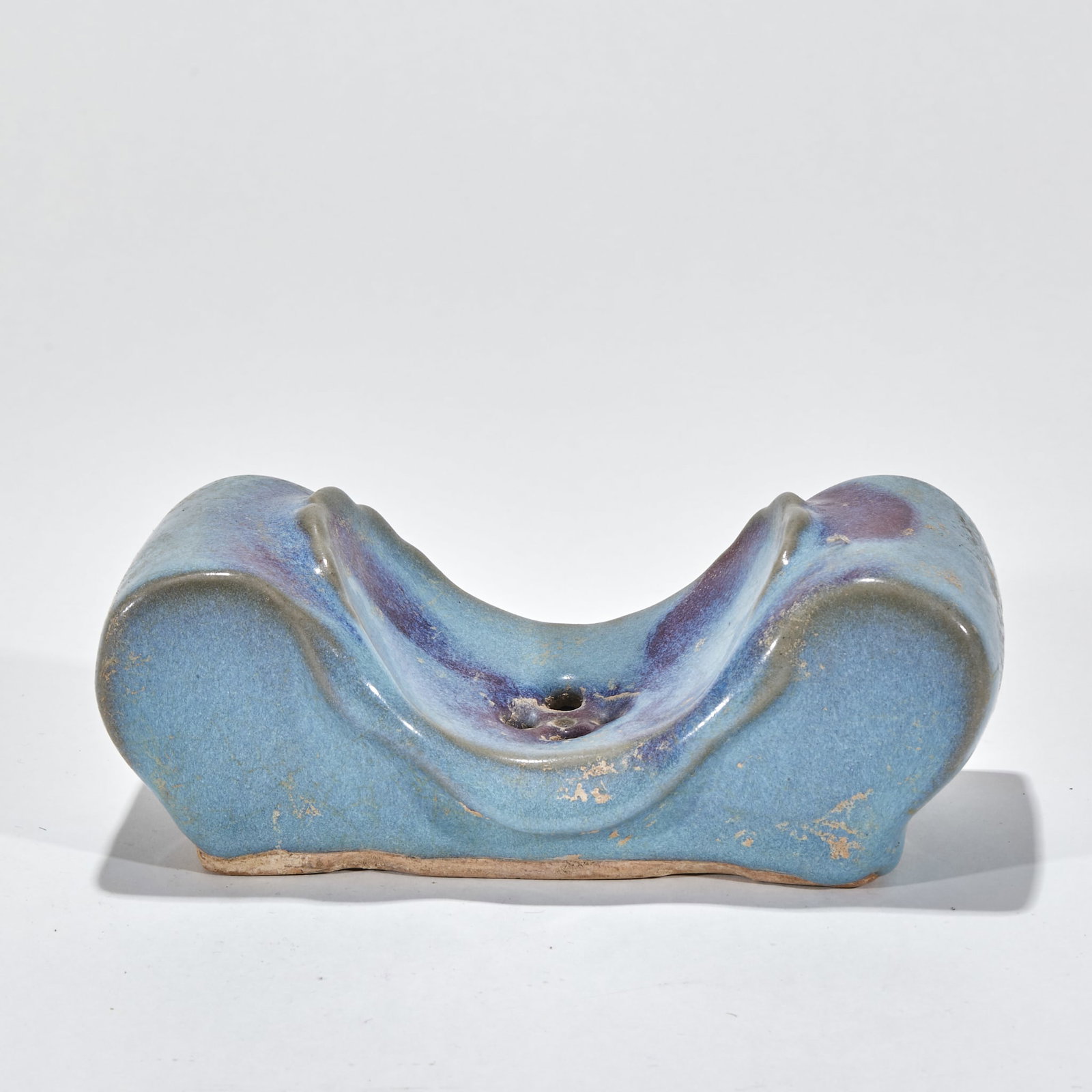 Jun kiln rose purple rectangular pillow: The holder is saddle-shaped, with high ends, concave middle part and a round hole in the center. Sky blue glaze is applied all over the body, the glaze surface is warm and moist, and local purple