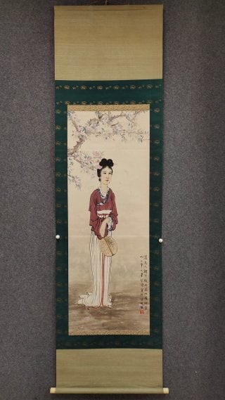 Xu Beihong's picture of a lady: Original vertical shaft, silk painting. Painted a lady in ancient costume, with a bun and flowers, dressed in a red coat and a long white dress, holding a group fan and standing under a peach tree.