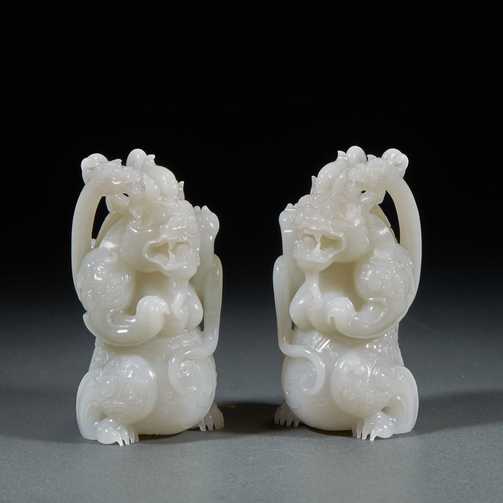 Hetian jade beast pair: Hetian white jade texture, paired furnishings. The beast is squatting, grinning, and imposing. The beast is covered with carved cirrus ornamentation, and its shoulders are wrapped with elegant ribbons