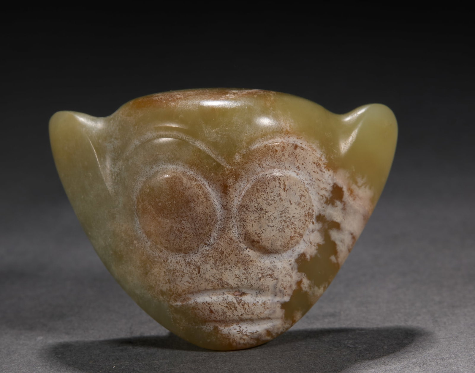 Hongshan jade face beast statue: Topaz texture, the overall shape is inverted triangle. The surface of the instrument is carved with the image of human face, the eye socket is convex, the eye contour is round, the intaglio lines show