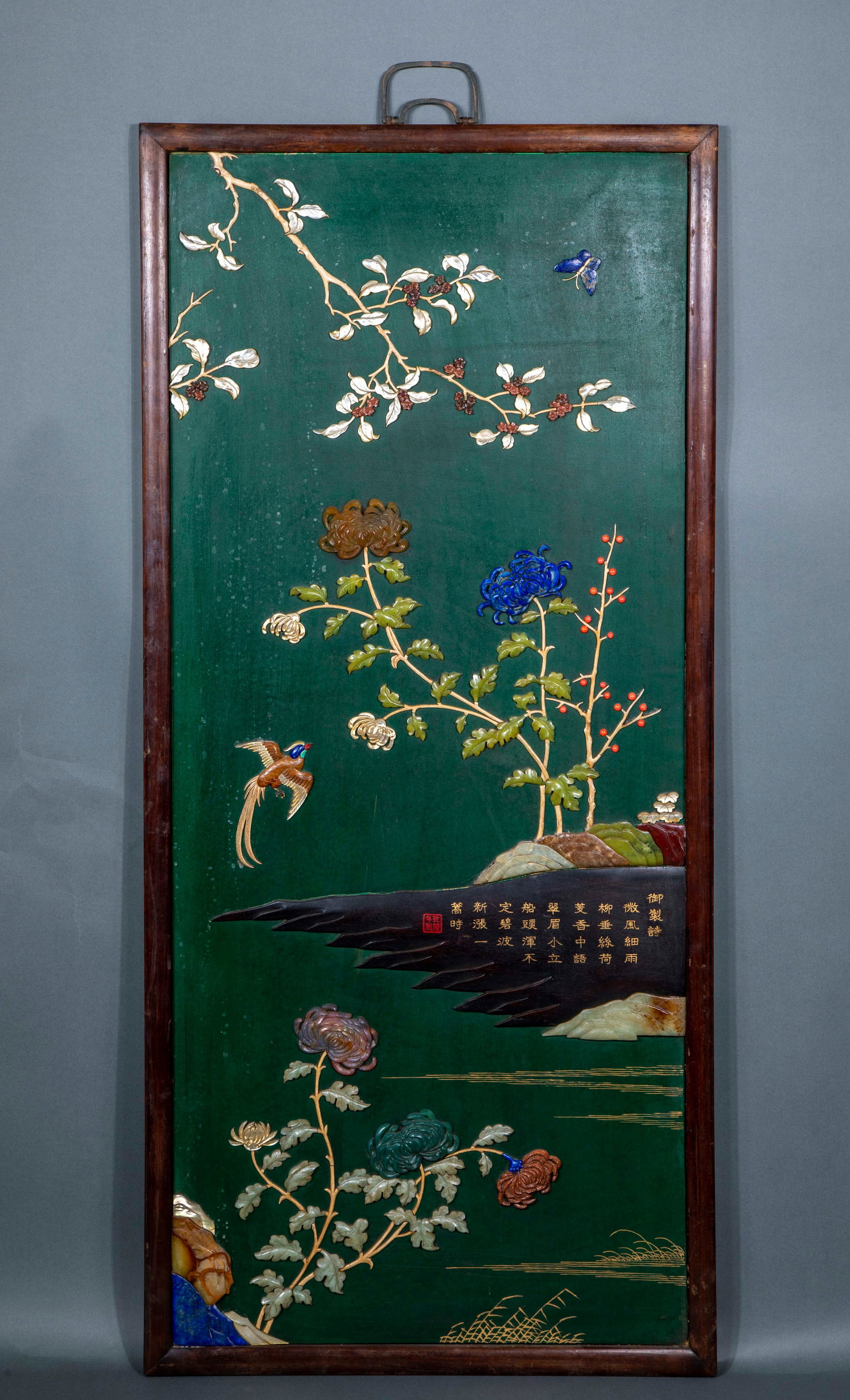Qingganlong rosewood inlaid with flowers and birds hanging screen: Rectangular hanging screen with hardwood frame. The screen center is painted in green, and the water surface of chrysanthemum, cuttlefish, birds, butterflies and rocks is inlaid with jade, agate, lapi